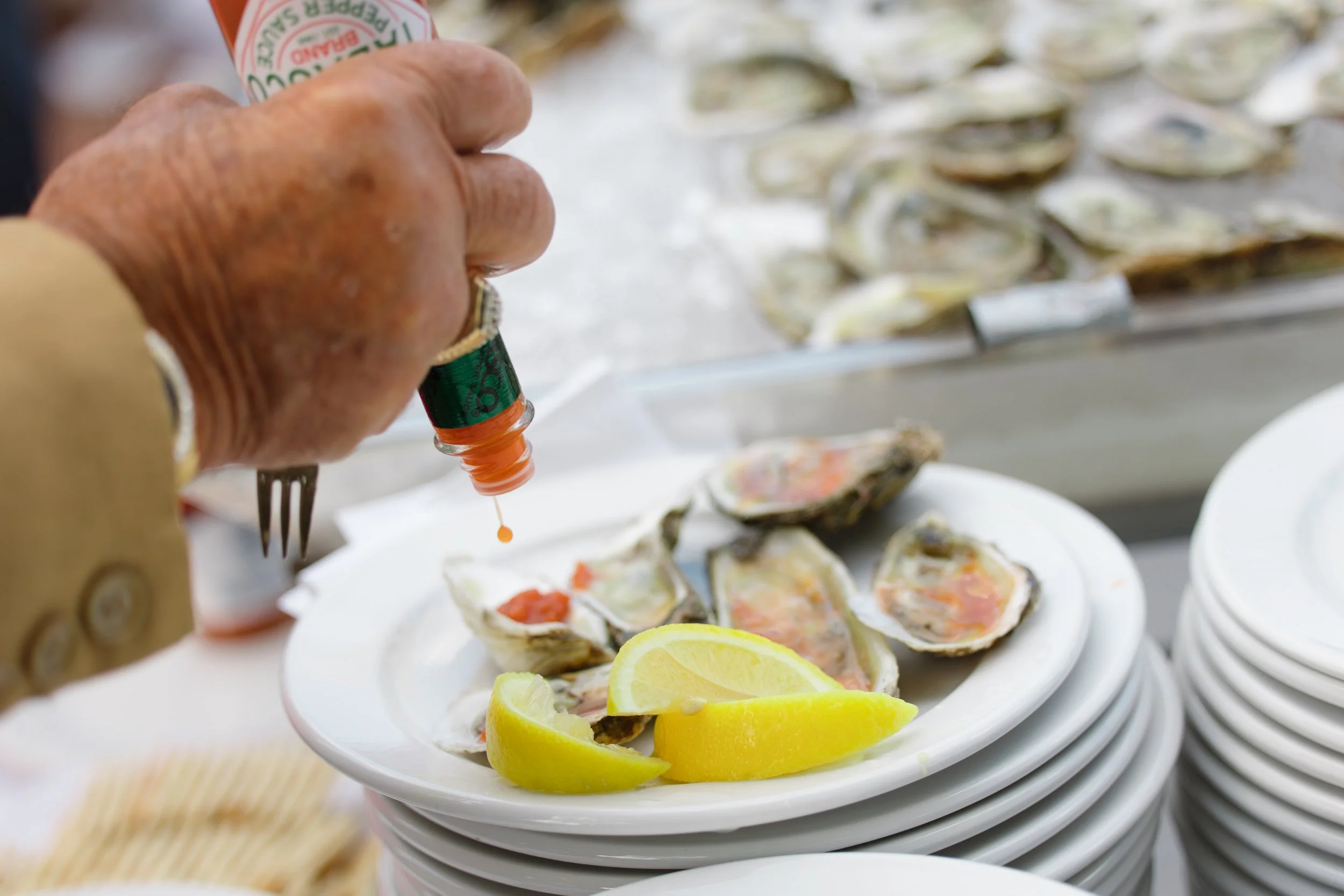 A person squeezing lemon onto a plate of raw oysters garnished with lemon wedges and a small container of hot sauce.