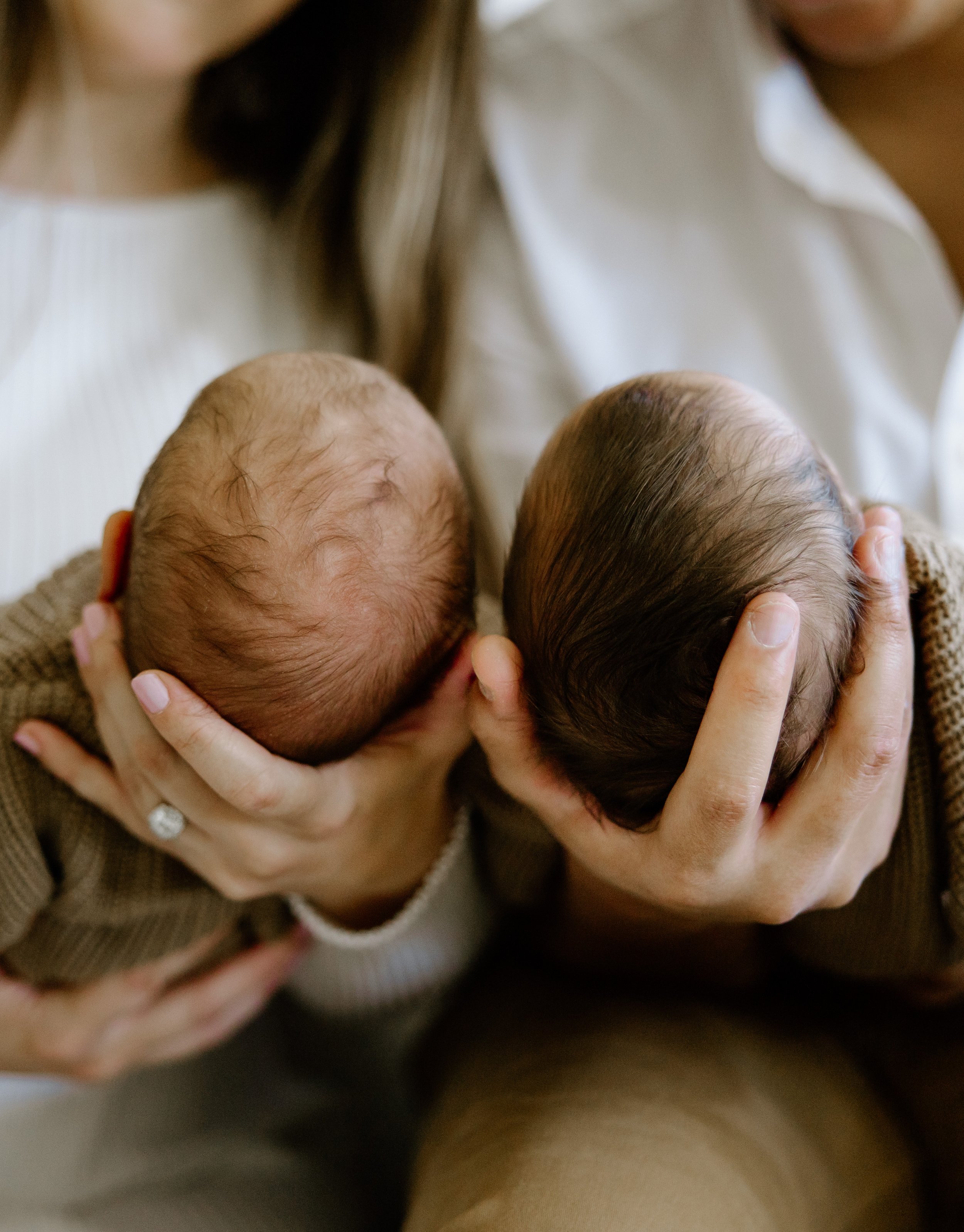Two infants with bald heads being held close by an adult, possibly a mother, in a tender moment.