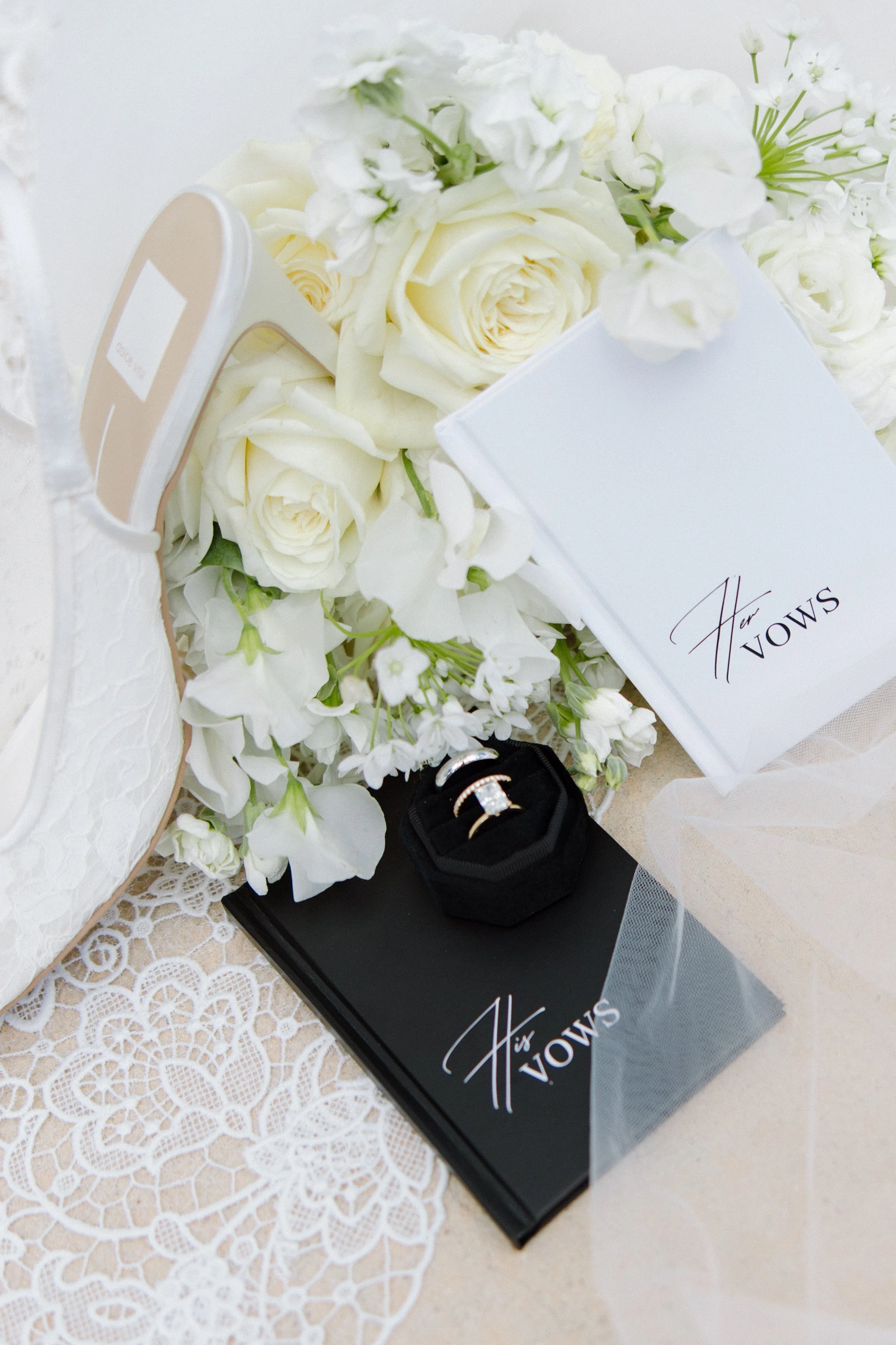 White roses and floral arrangements, a jewelry box with rings, a card with a signature, on a lace tablecloth.