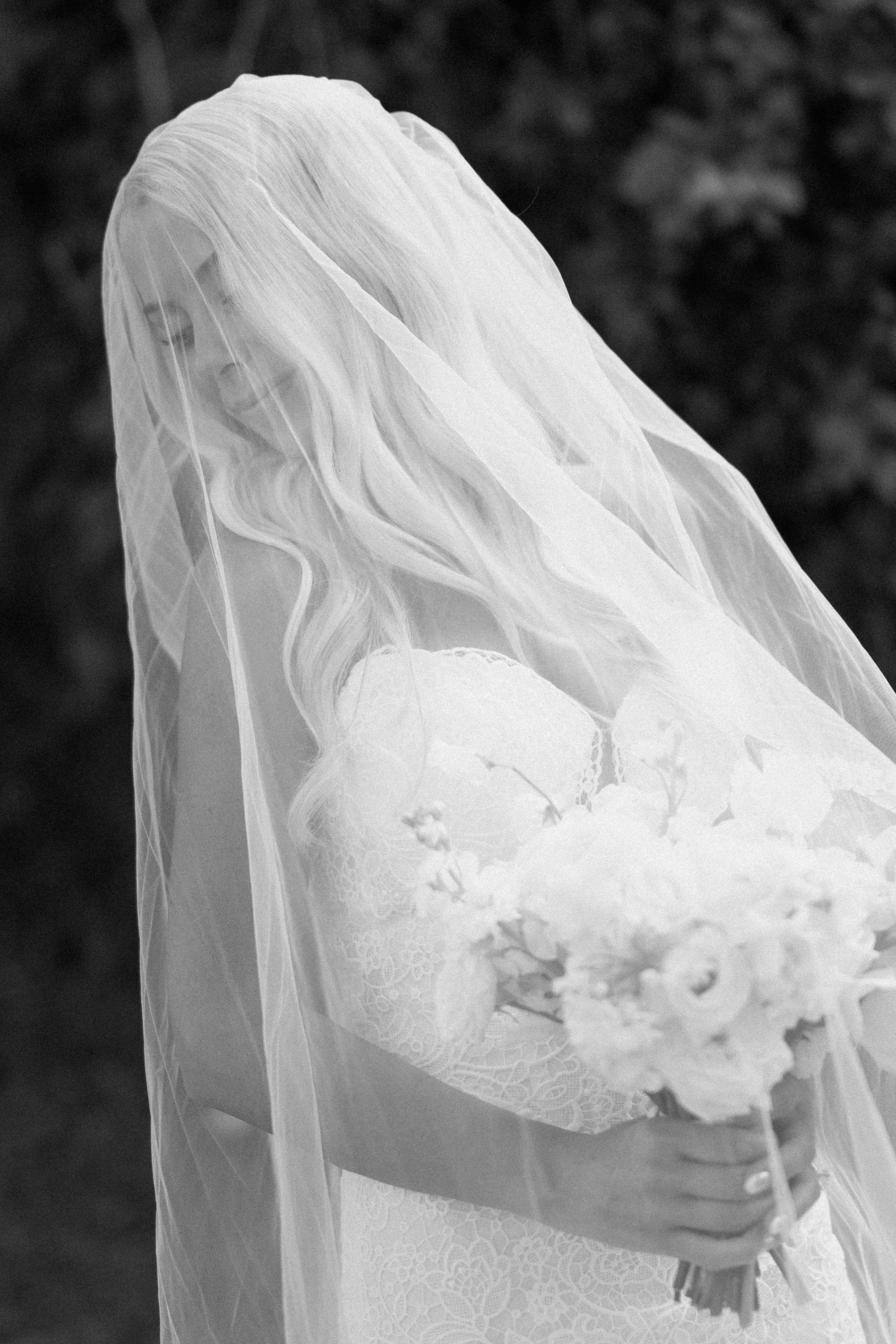 A bride in a wedding dress with a veil holding a bouquet of flowers.