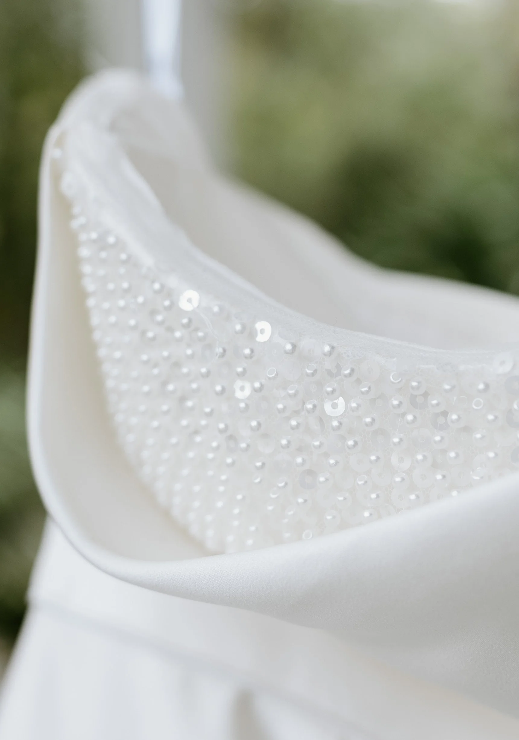 Close-up of a white fabric with decorative beads and sequins, possibly part of a wedding dress or elegant clothing.
