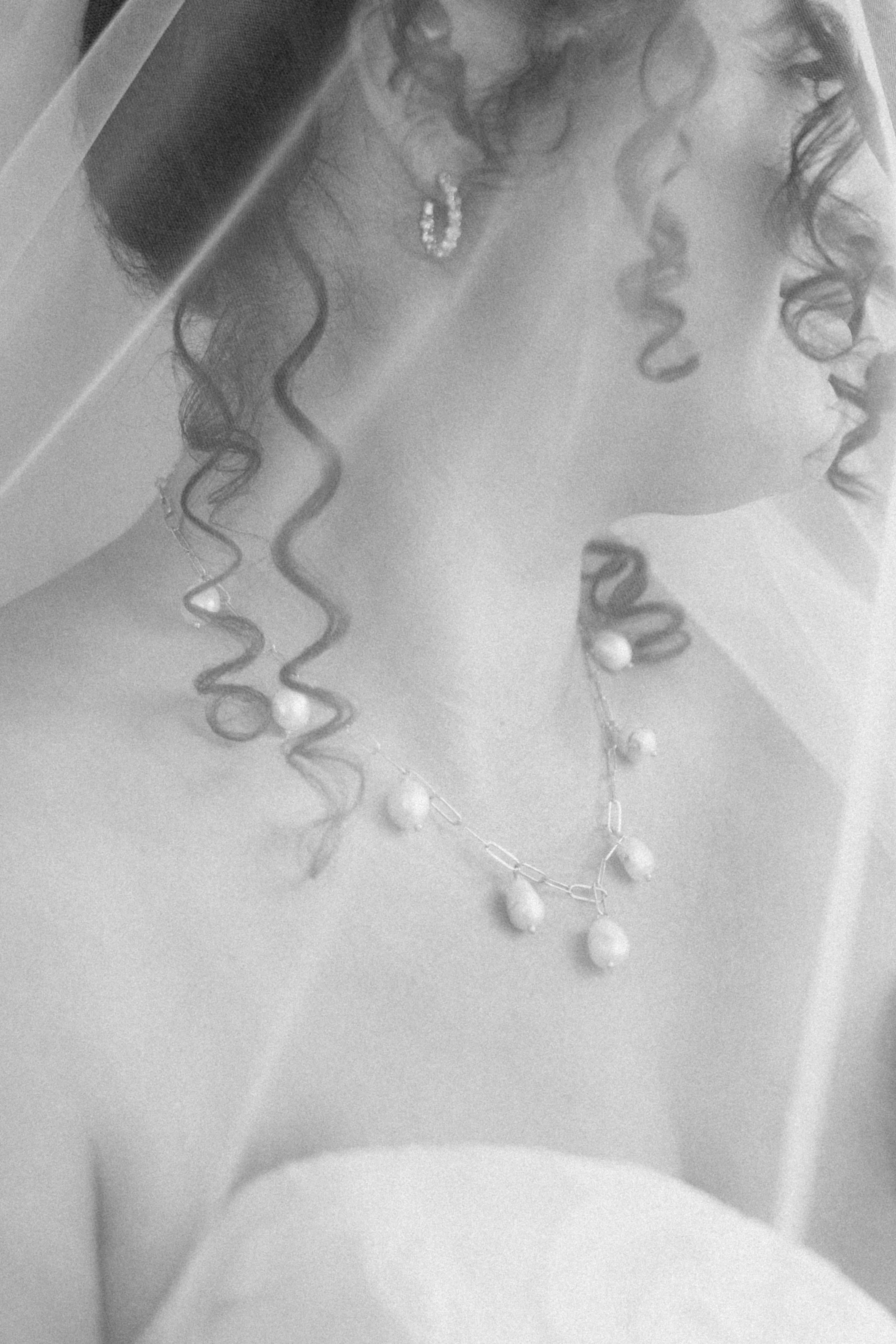 A woman wearing curly hair and glasses, adorned with jewelry, appears to be taking a selfie or pose with her face close to the camera.