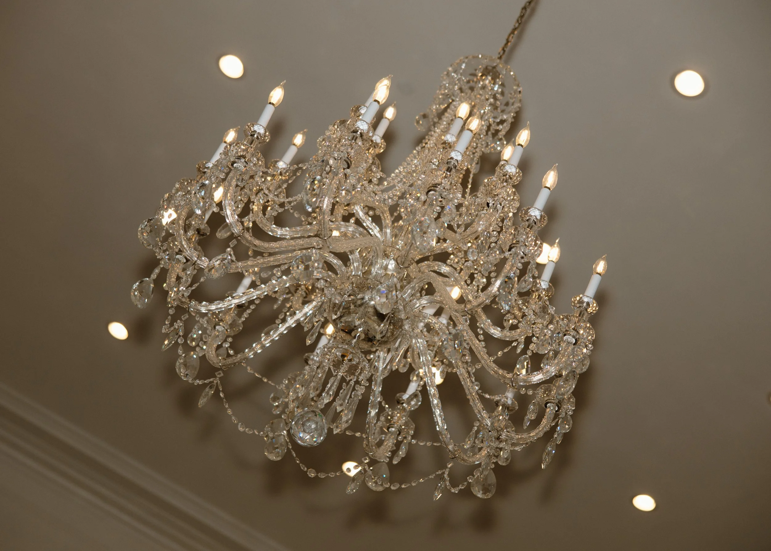 A crystal chandelier hanging from the ceiling with lit candle-shaped bulbs and reflective glass/crystal decorations.