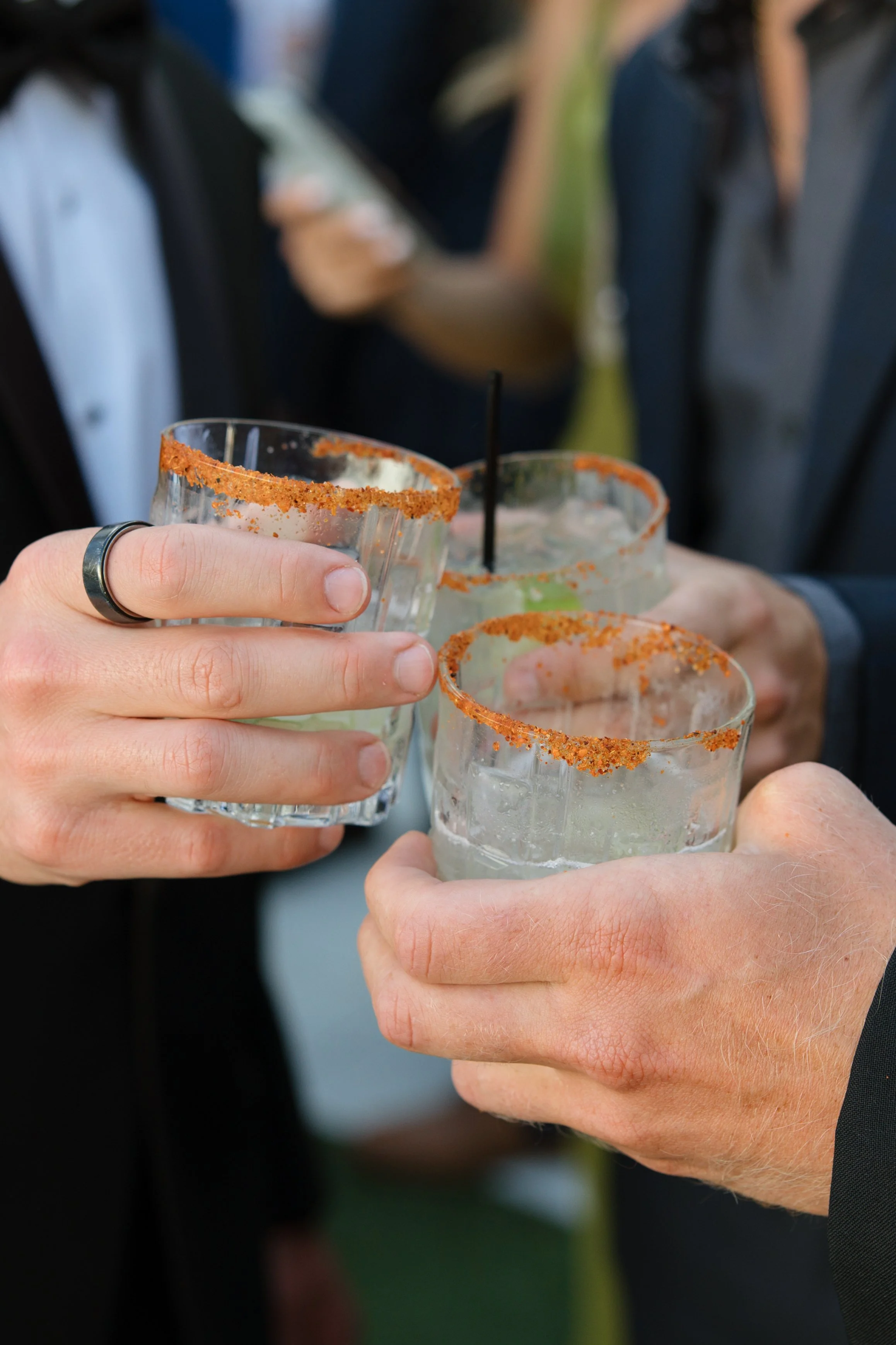 Close-up of several people holding margarita glasses with salted rims, toasting at an outdoor gathering.