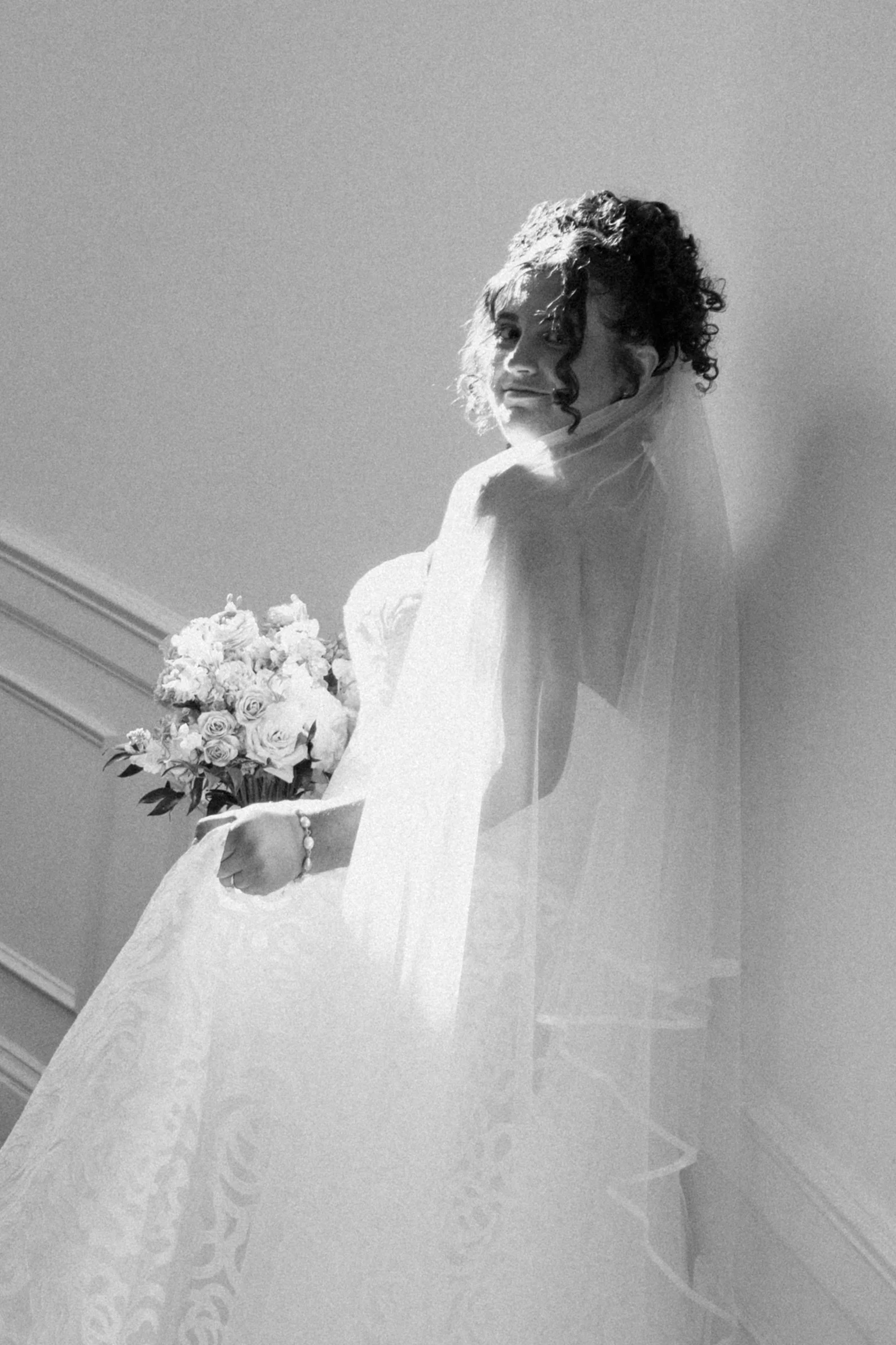 Black and white photo of a woman in a wedding dress holding a bouquet of flowers, looking over her shoulder.