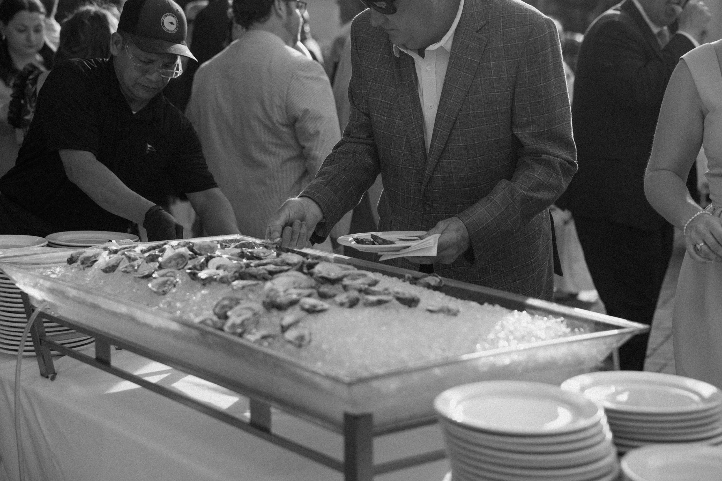 People serving and selecting food at a buffet with seafood on a large tray.