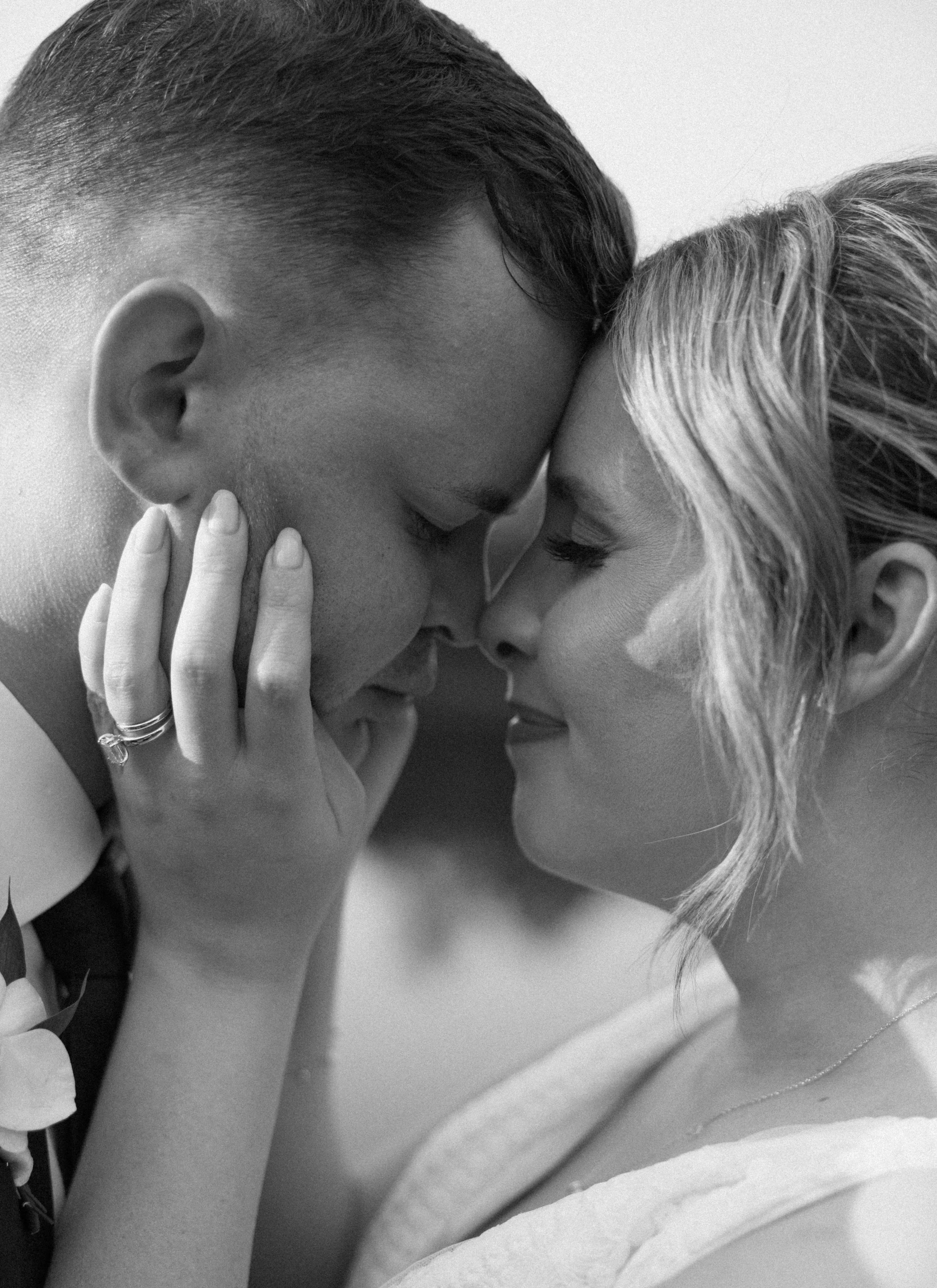 A black and white close-up of a couple touching foreheads and eyes closed, showing intimacy and affection.
