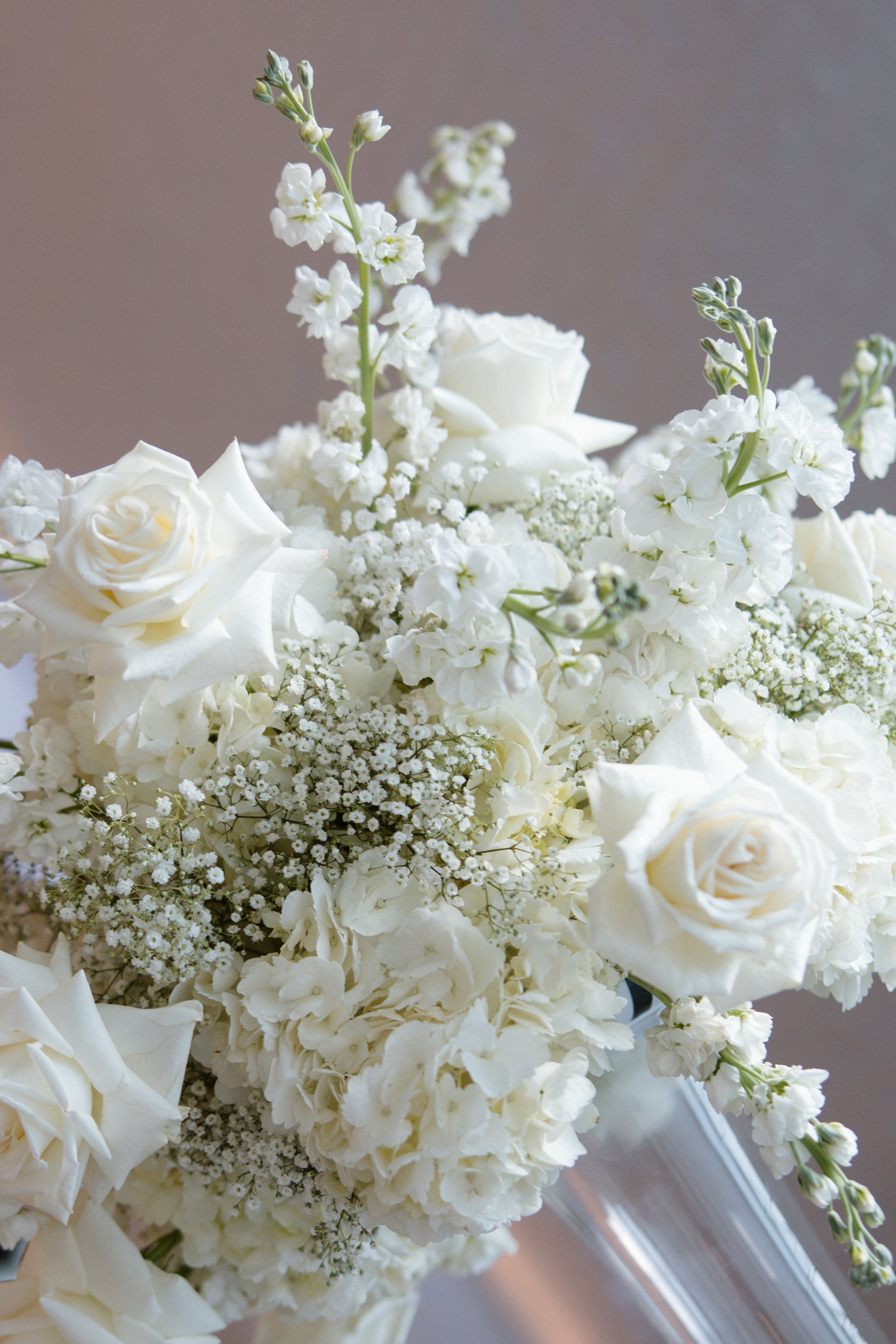 Close-up of a bouquet of white flowers, including roses, hydrangeas, and other small blooms, in a clear glass vase.