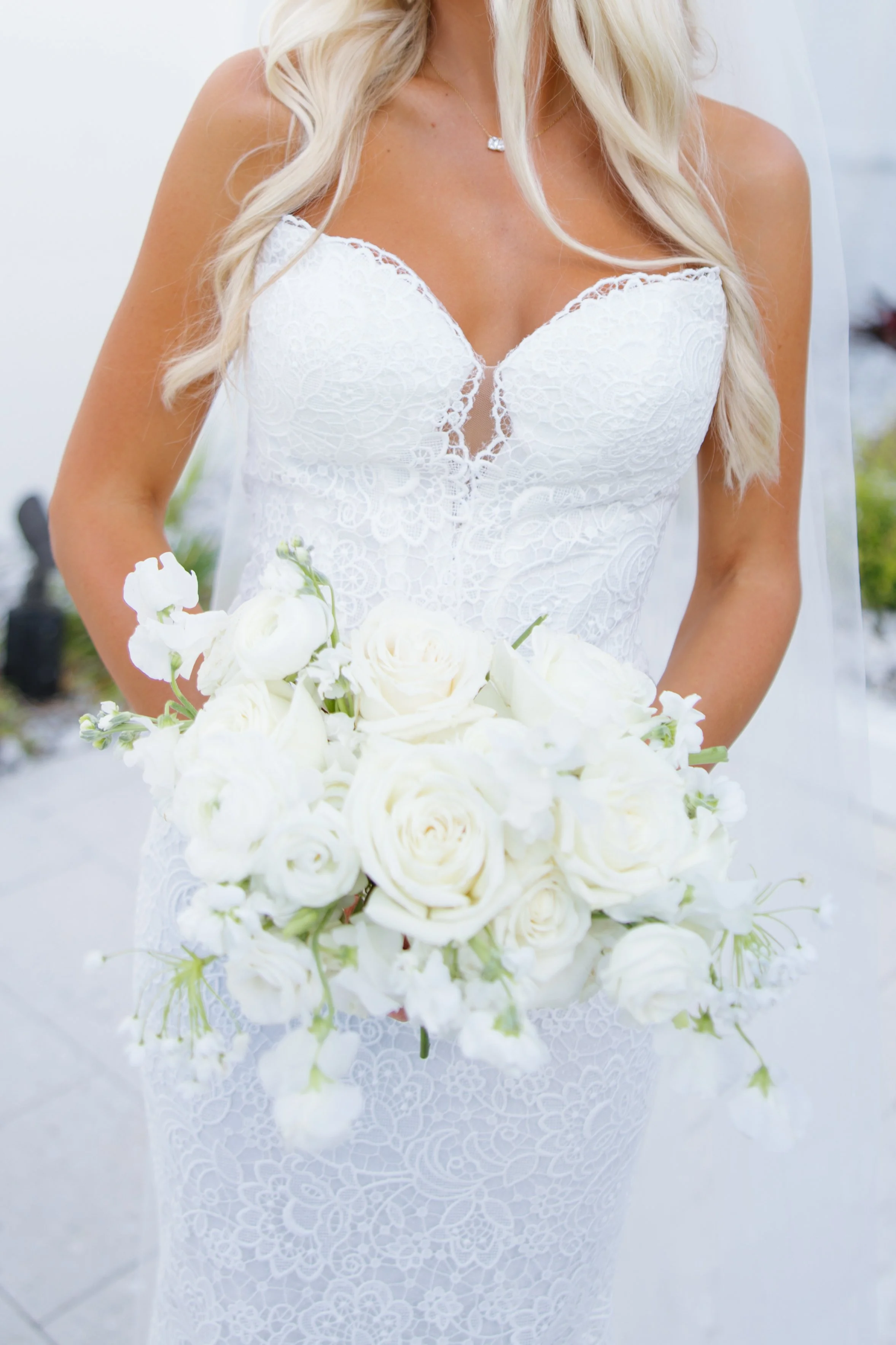 A woman in a white lace dress holding a bouquet of white roses and greenery.