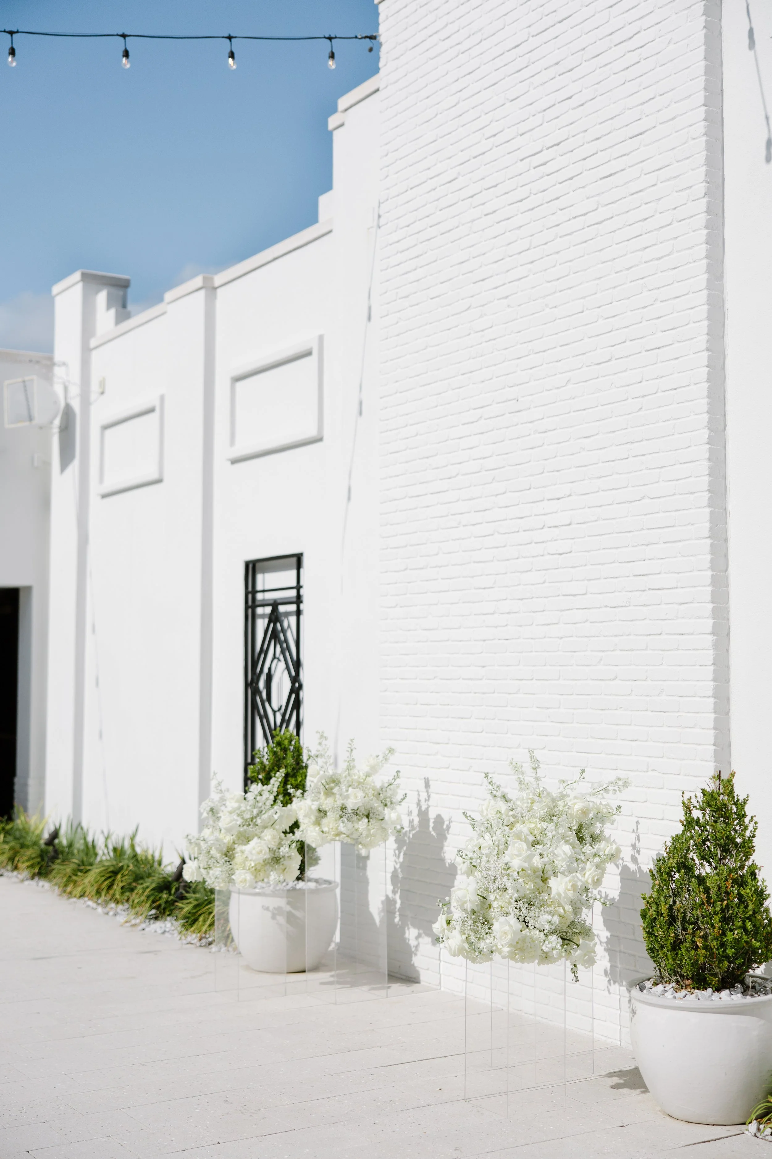 White building with a brick wall and decorative flowers in pots