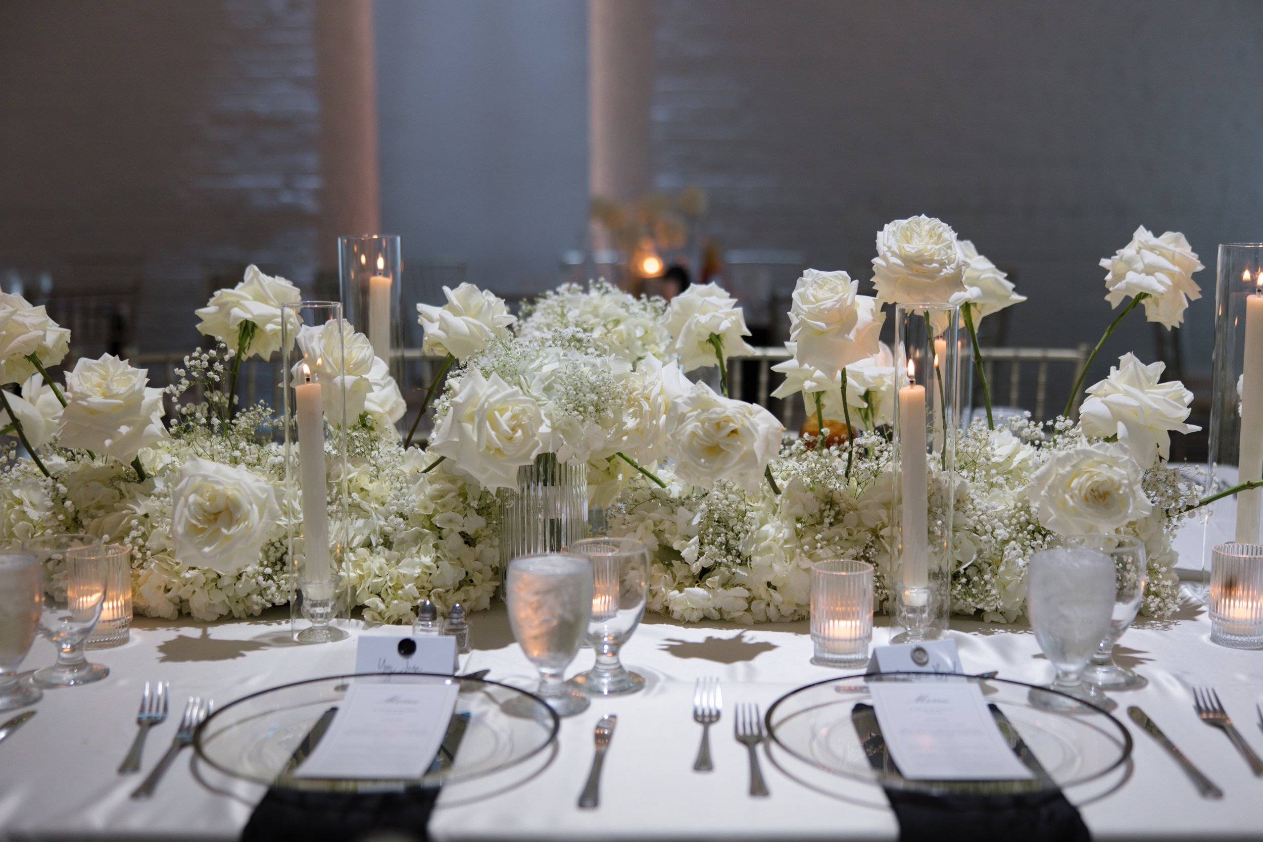 Elegant table setting with white roses and tall candles at a formal event or wedding reception.