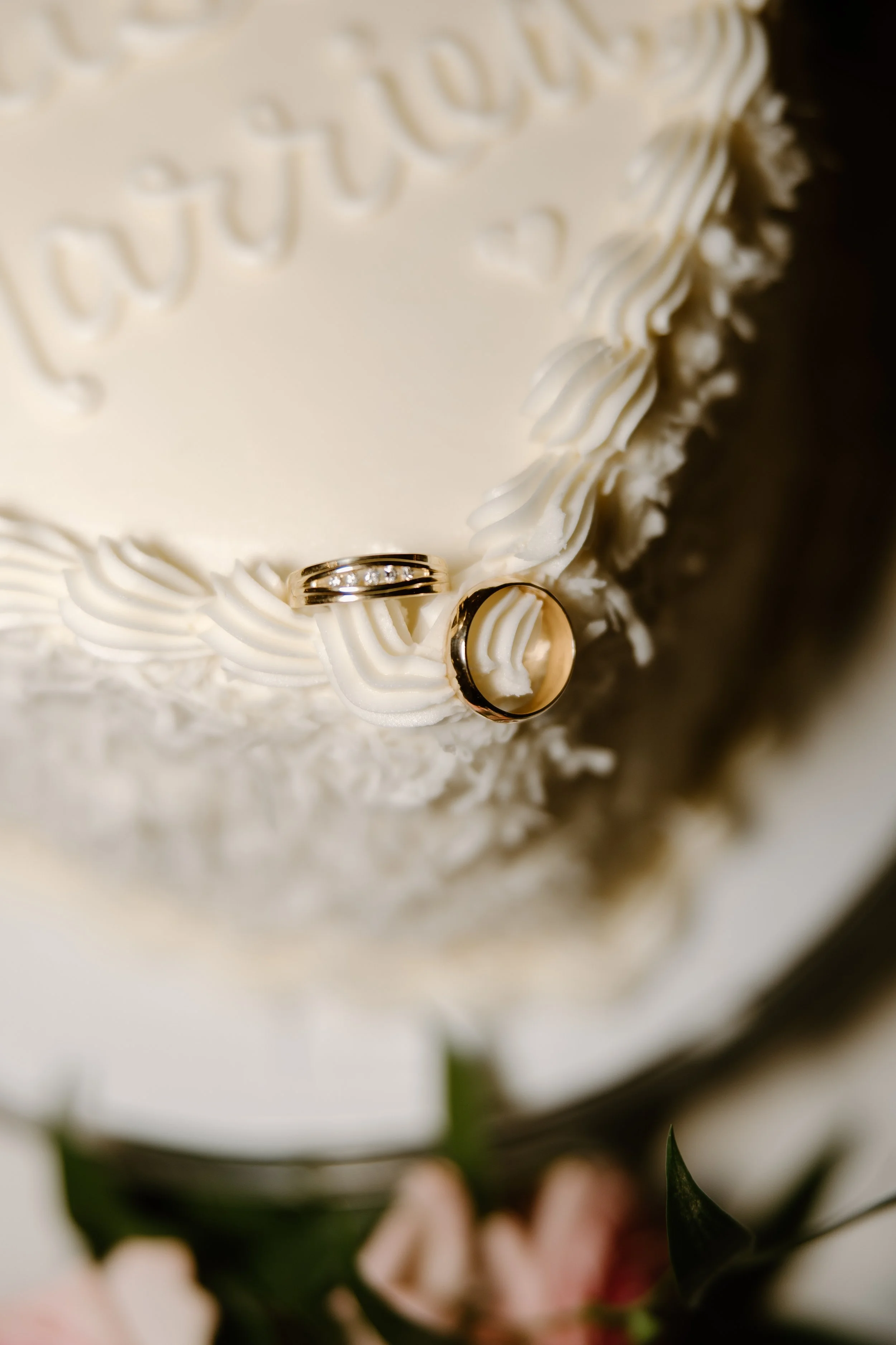 Close-up of a wedding cake with wedding bands and white frosting decorating the top.