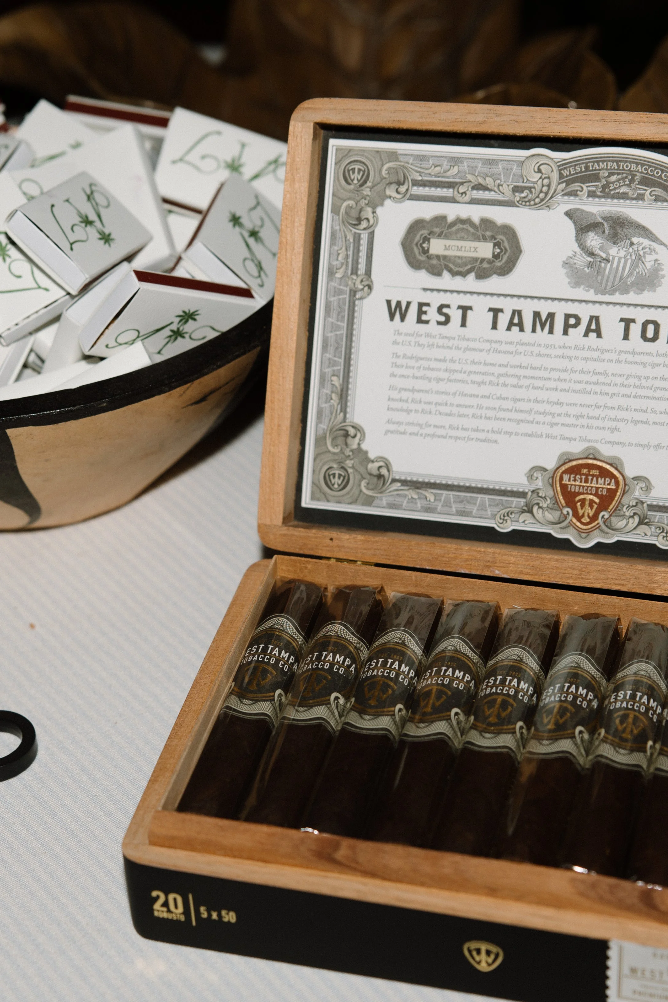 Open wooden box containing cigars labeled 'West Tampa Tobacco Co.' and a sign with the same branding.