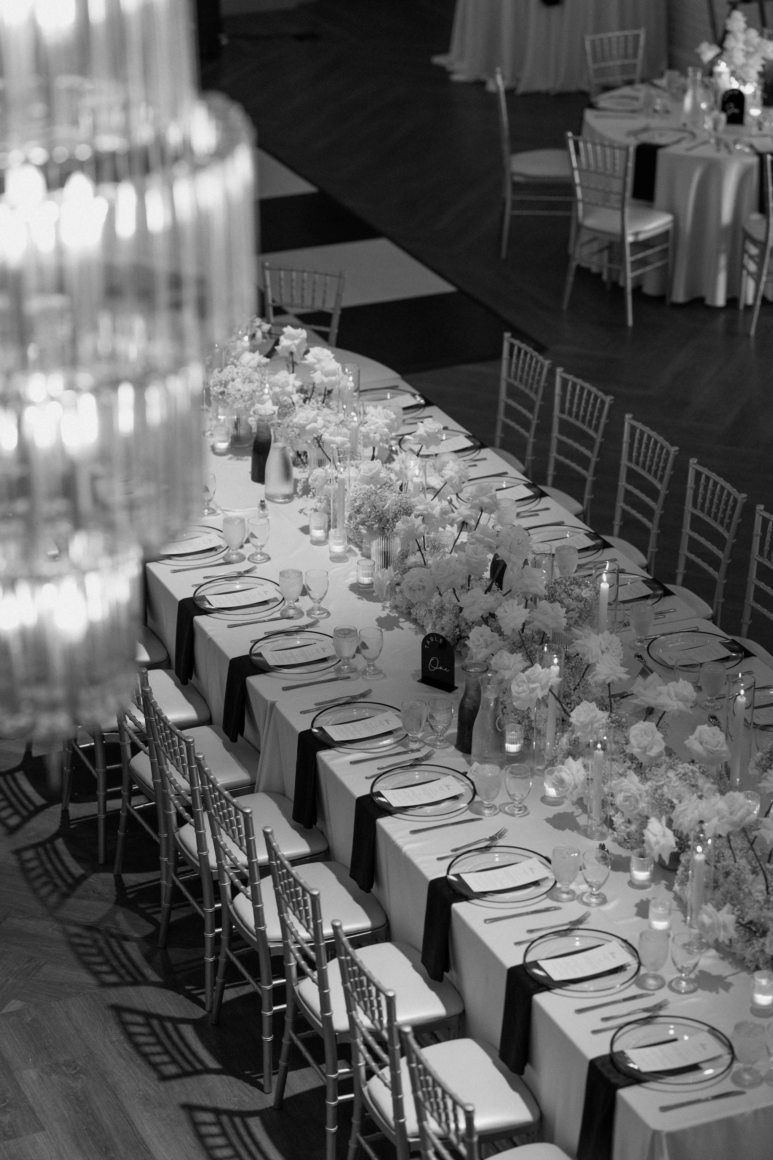 Long banquet table decorated with white flowers, candles, and place settings, arranged for a formal dinner at an event venue.