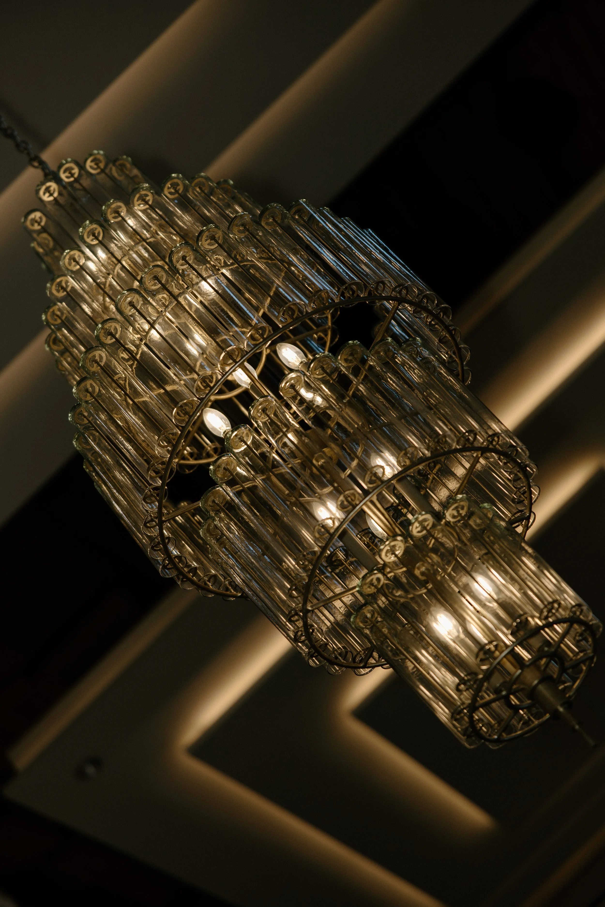 Close-up view of a chandelier with multiple glass tubes and small light bulbs, hanging from a ceiling with recessed lighting.
