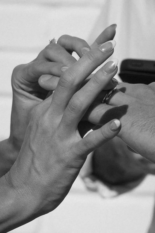 Close-up of two hands with intertwined fingers, one hand with a ring on the ring finger, in a black and white photo.