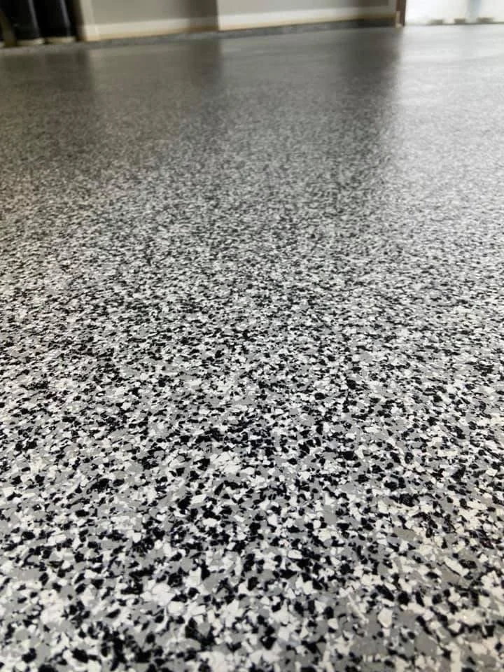 Close-up of a speckled black, white, and gray terrazzo floor in an indoor space with a door in the background.