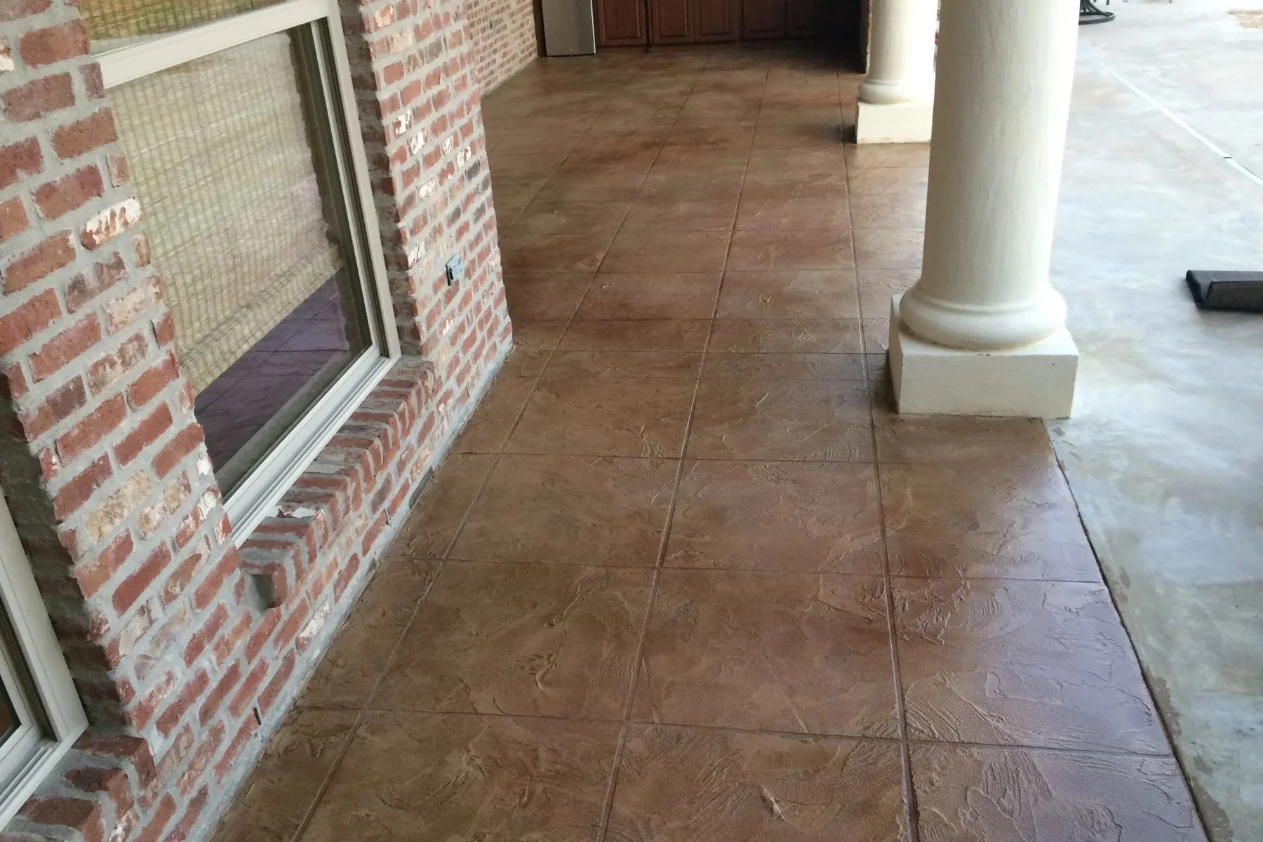 Trowel texture concrete overlay with a stone-look finish on a covered porch of a brick home