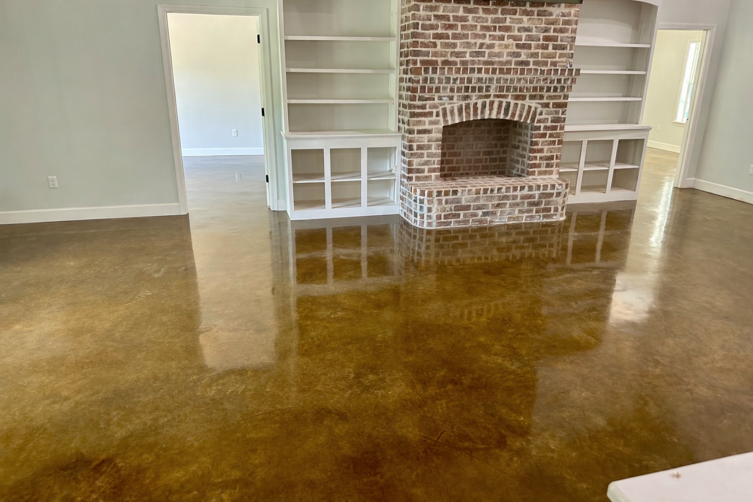 Living room with polished concrete floor, white walls, and a brick fireplace with built-in white shelves on both sides.