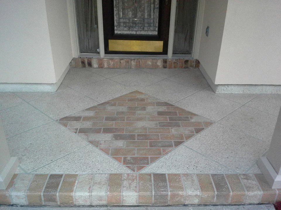 Front porch with a diamond-shaped brick pattern surrounded by concrete flooring and a sliding glass door with a screen door.