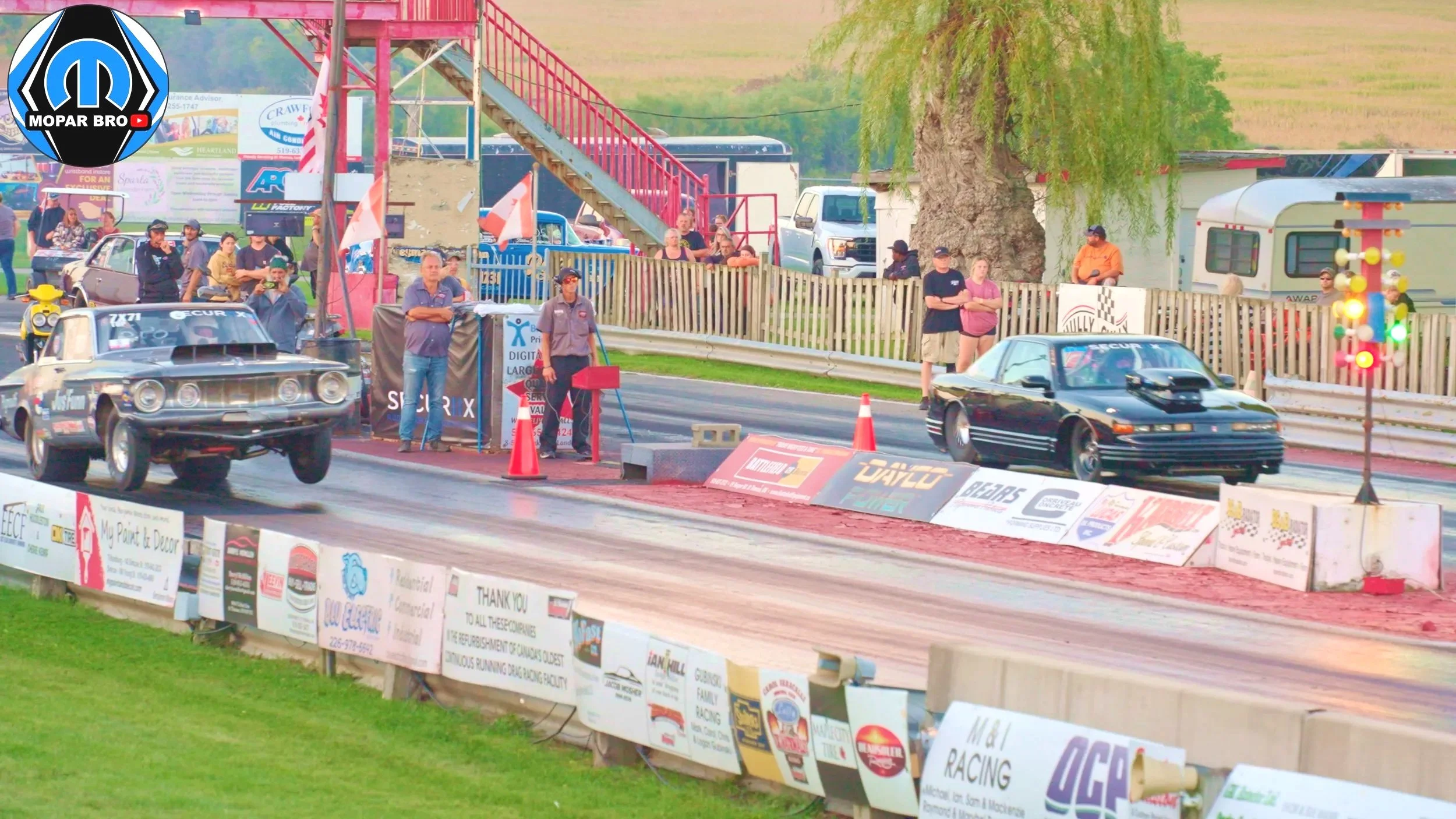 st thomas dragway drag racing Two drag racing cars on a track with people watching in the background, safety cones, and illuminated starting lights. Plymouth Fury Drag race