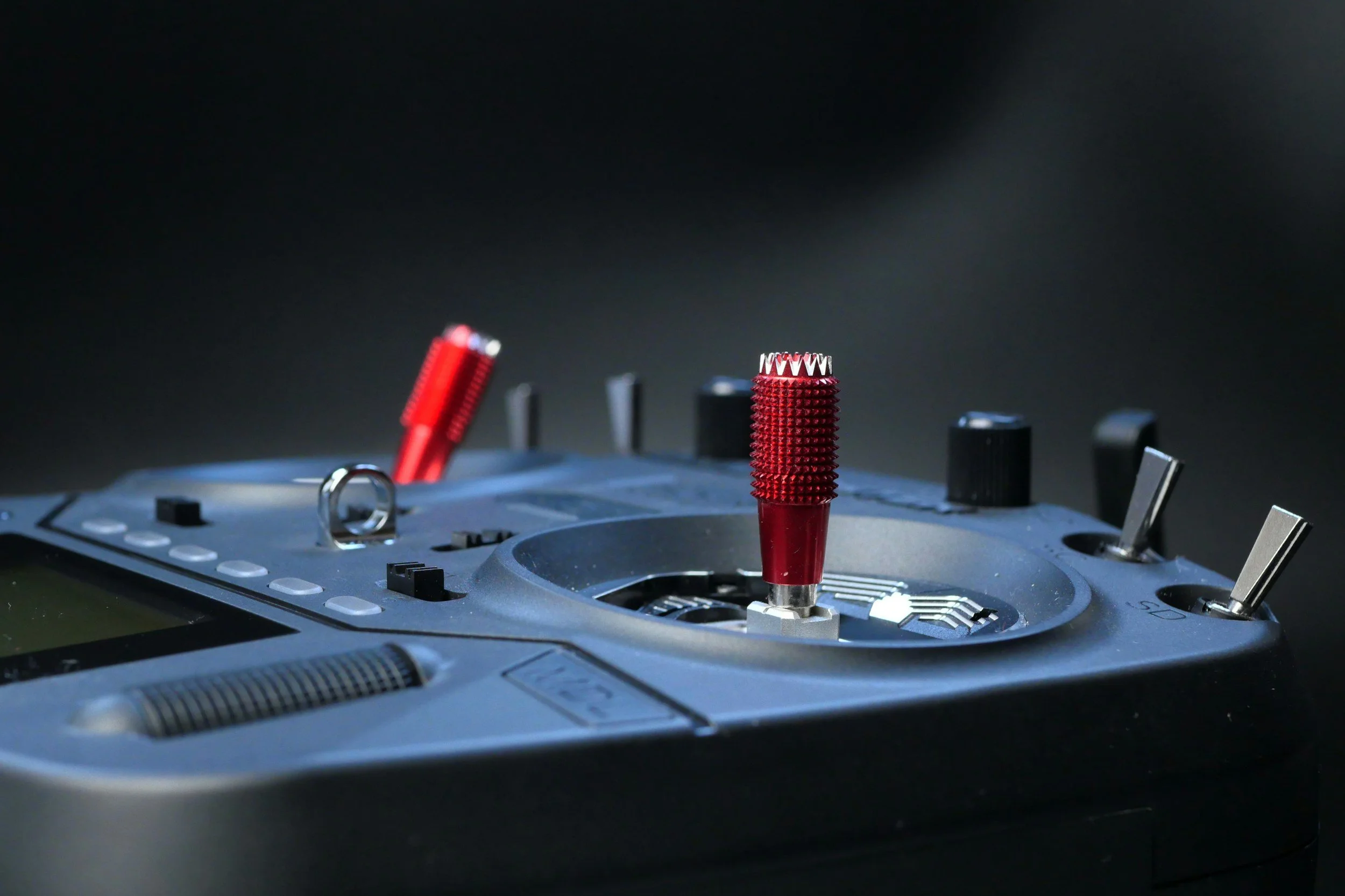 Close-up of a FPV Drone controller with two red grips on the jog wheels, set against a dark background.
