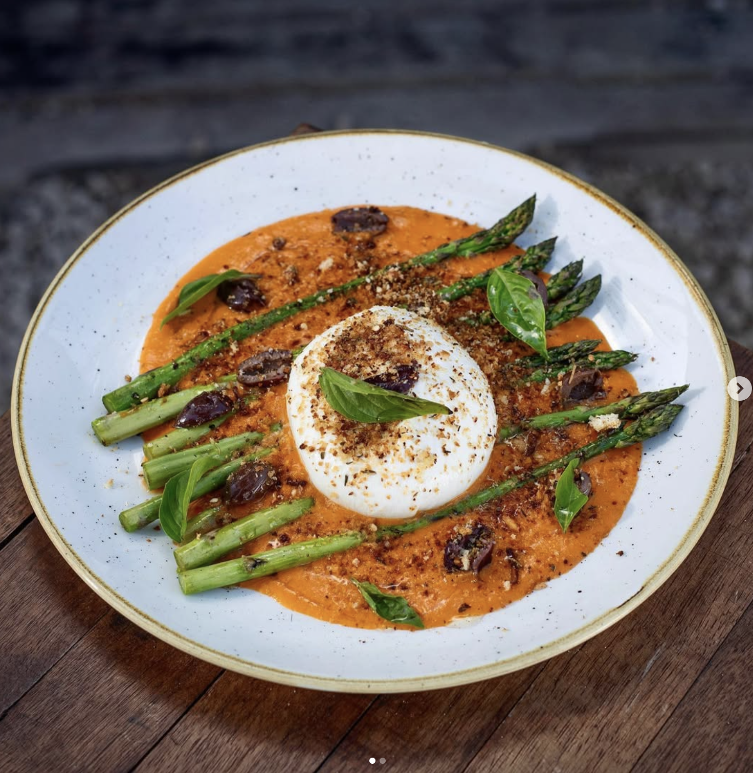 Plato con huevo cocido, espárragos, hojas de albahaca, aceitunas y salsa de tomate.