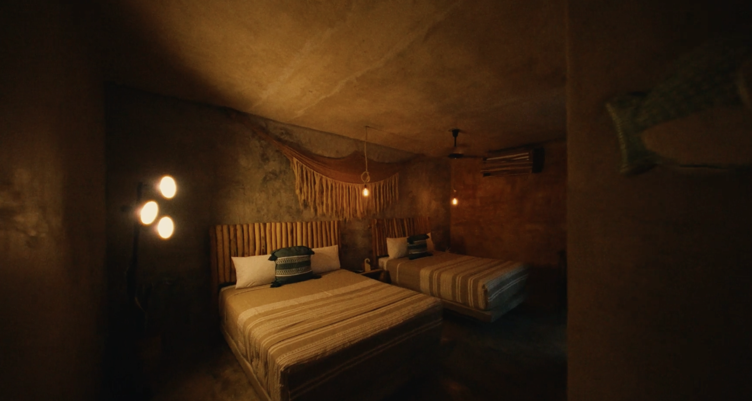 Dos camas con cabeceras de madera en una habitación con paredes de piedra, decorada de manera rústica, con iluminación cálida y lámparas colgantes.