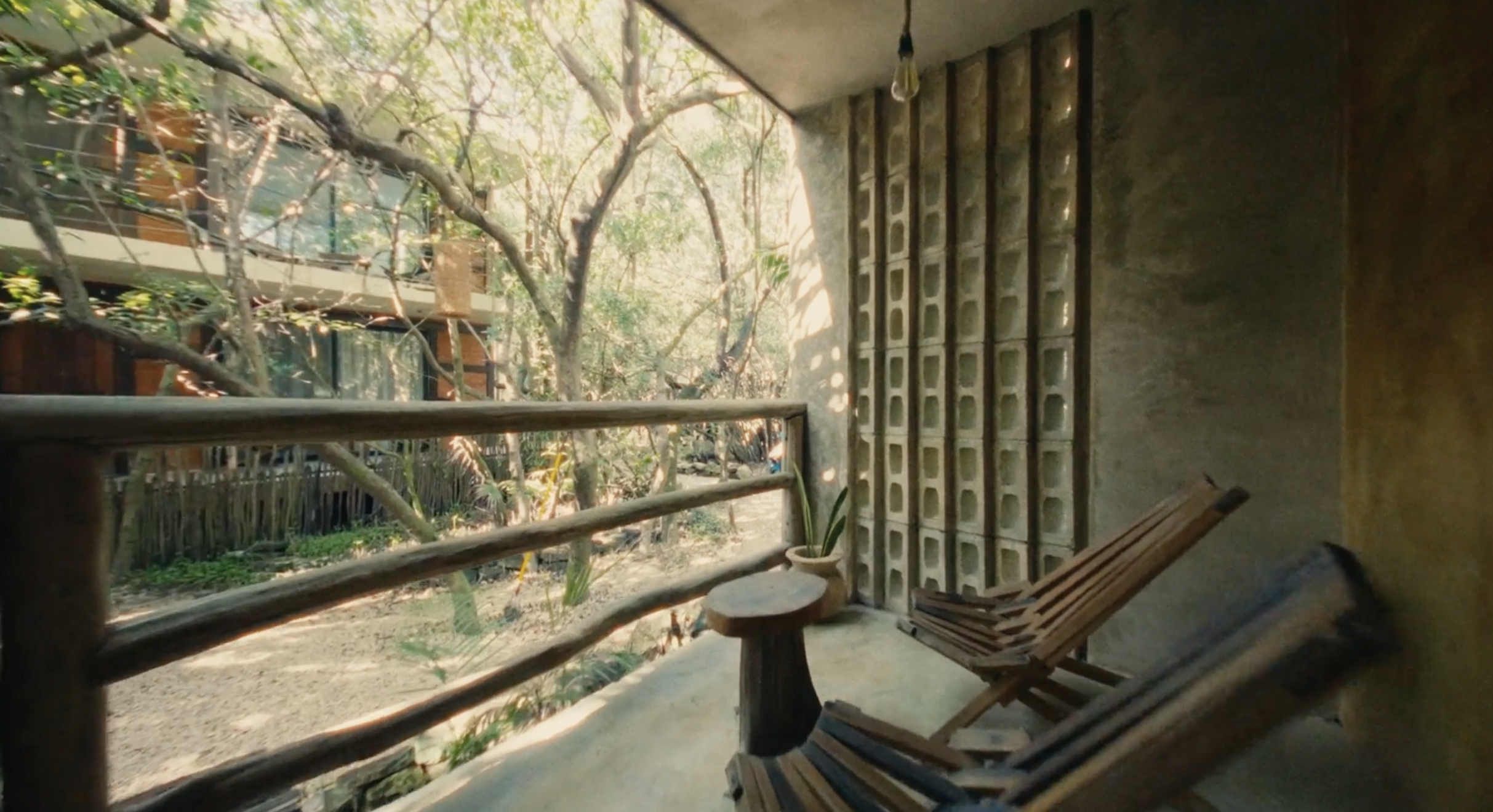 Vista desde un balcón con dos sillas de madera y una maceta con planta, rodeado de árboles y naturaleza