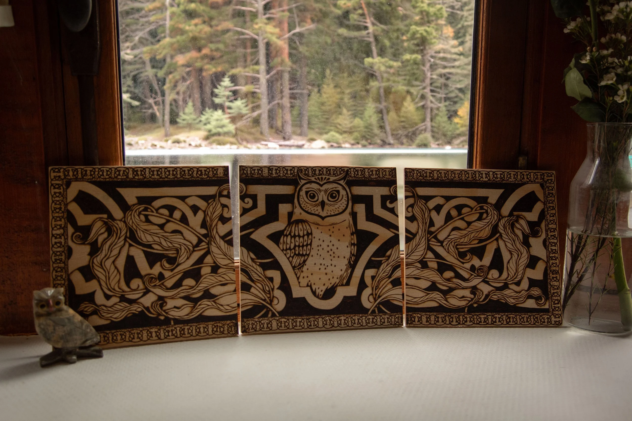 Triptyque mural en bois composé de trois panneaux pyrogravés à la main, représentant un hibou mystique entouré d'ornements et de motifs végétaux.