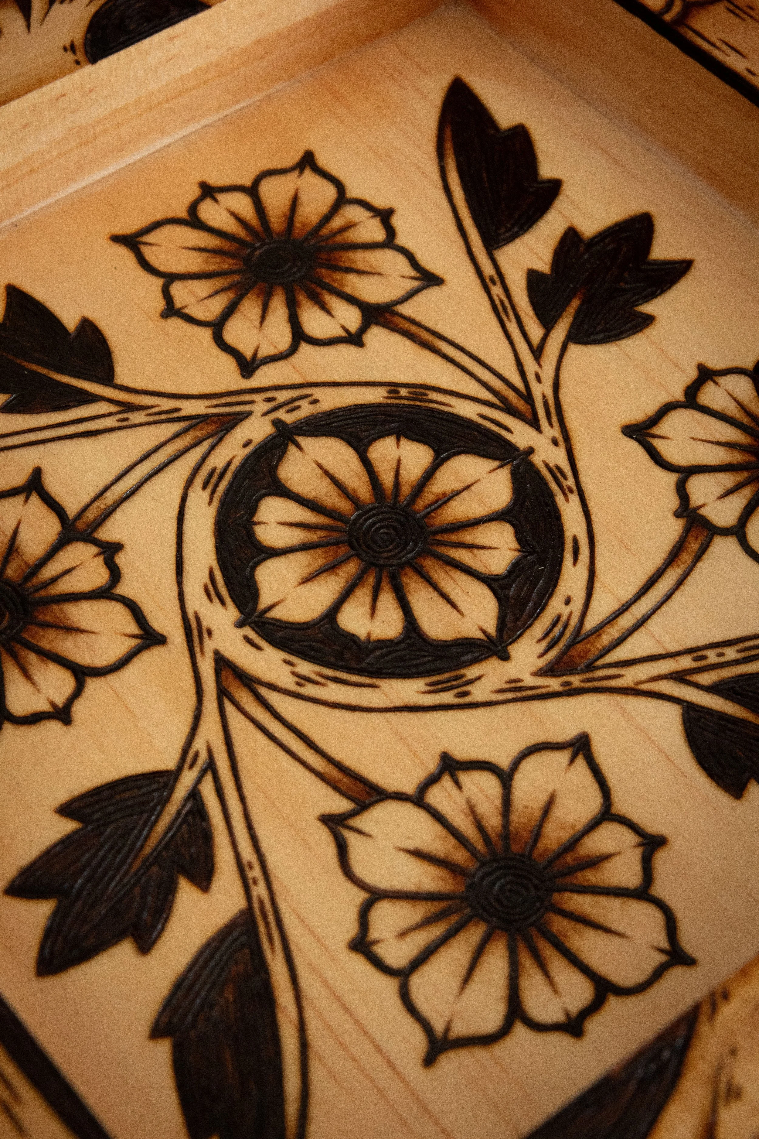 Zoom sur un plateau vide-poche carré en bois clair pyrogravé à la main avec des motifs de fleurs, d'entrelacs celtiques, d'un soleil et d'un croissant de lune mystique.