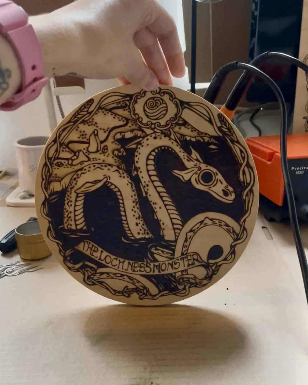 Pyrogravure artisanale ronde sur bois représentant la silhouette mystique du monstre du Loch Ness sous les eaux sombres d'Écosse.