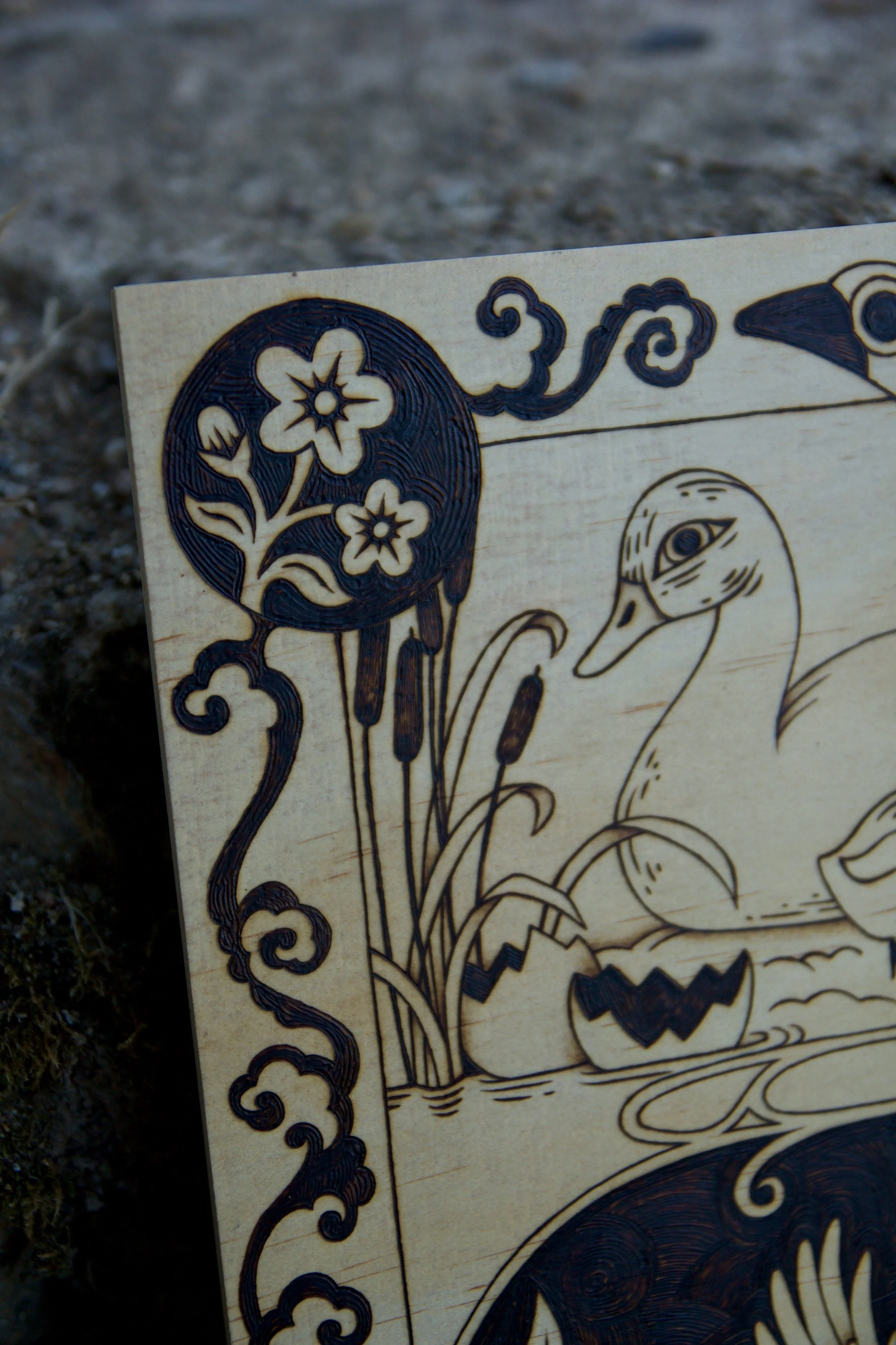 Détail symbole du printemps sur une plaque carrée en bois pyrogravé illustrant le conte du vilain petit canard en deux scènes avec entrelacs celtiques et symboles des saisons.