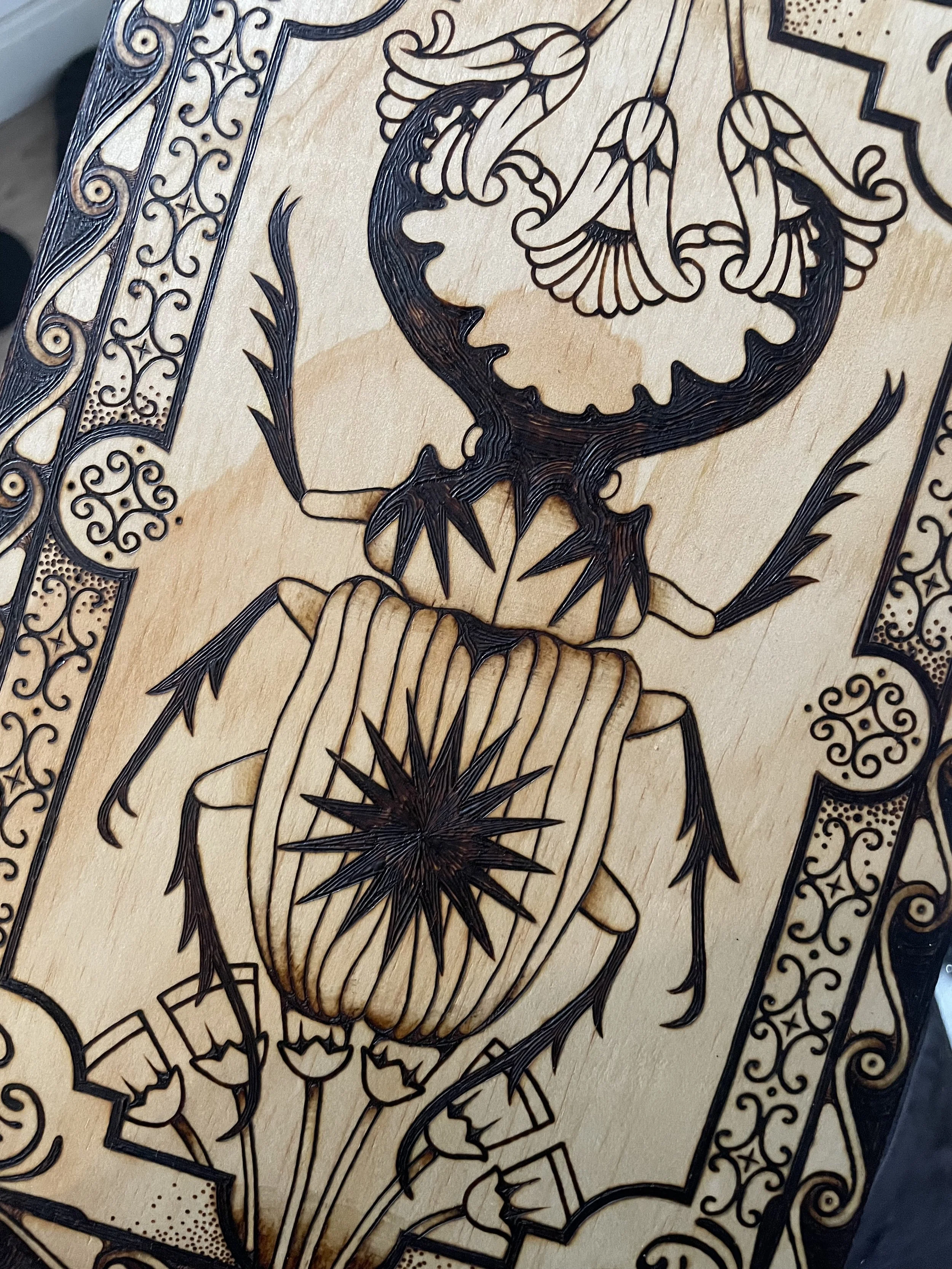 Détail d'une plaque en bois artisanale pyrogravée à la main représentant un scarabée sacré entouré de symboles anciens et de motifs ésotériques géométriques.