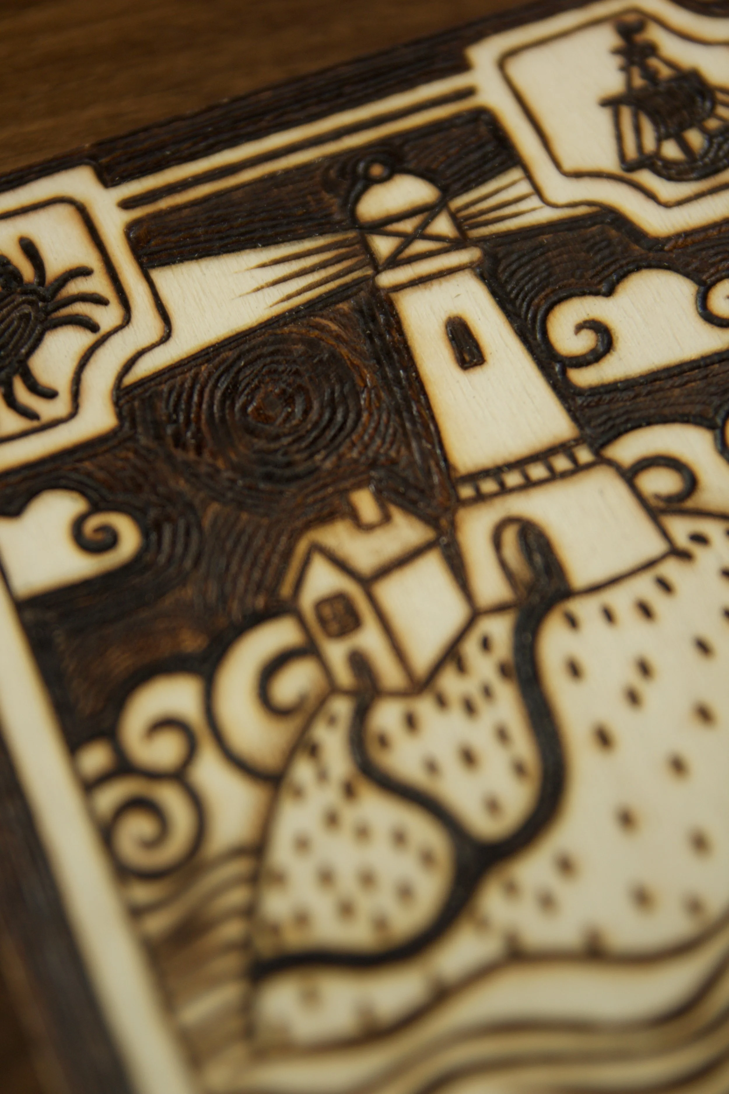 Zoom sur le phare d'une illustration d'une petite plaque en bois gravée à la main de motifs marins et de vagues, sertie d'une pierre d'agate bleue naturelle aux reflets aquatiques.