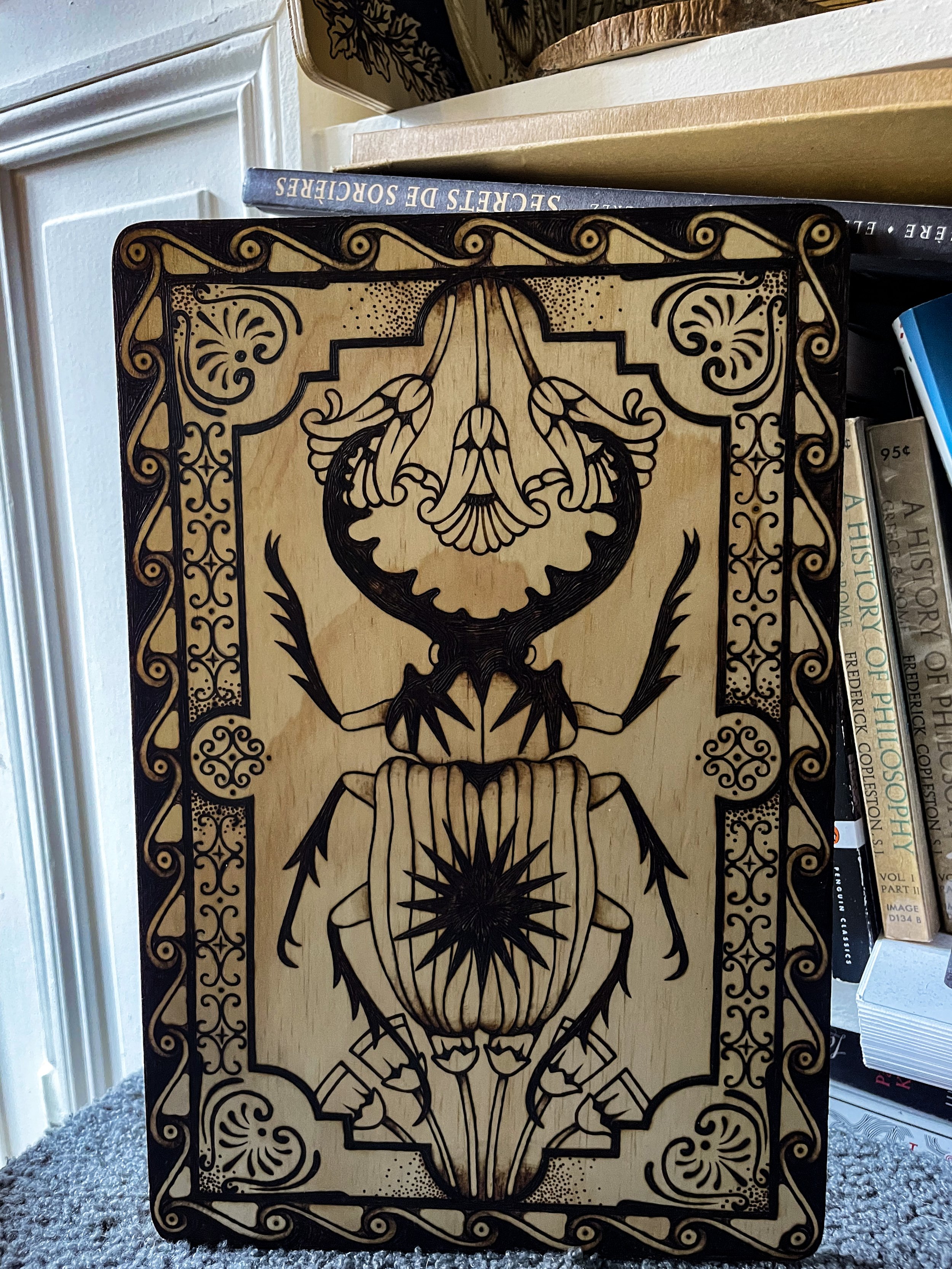 Plaque en bois artisanale pyrogravée à la main représentant un scarabée sacré entouré de symboles anciens et de motifs ésotériques géométriques devant une bibliothèque.