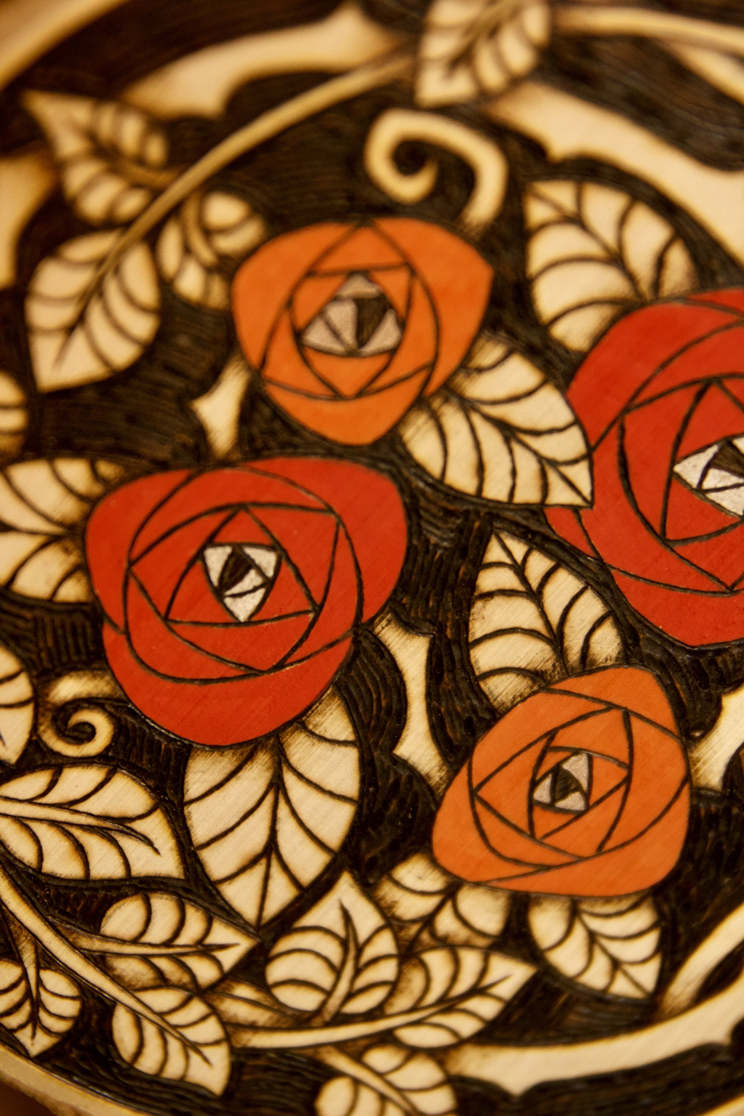 Détail sur la partie peinte rouge vif d'une amulette murale ronde en bois pyrogravé et peint avec des roses rouges, ornée de pendants en pierre et d'une rose en céramique.