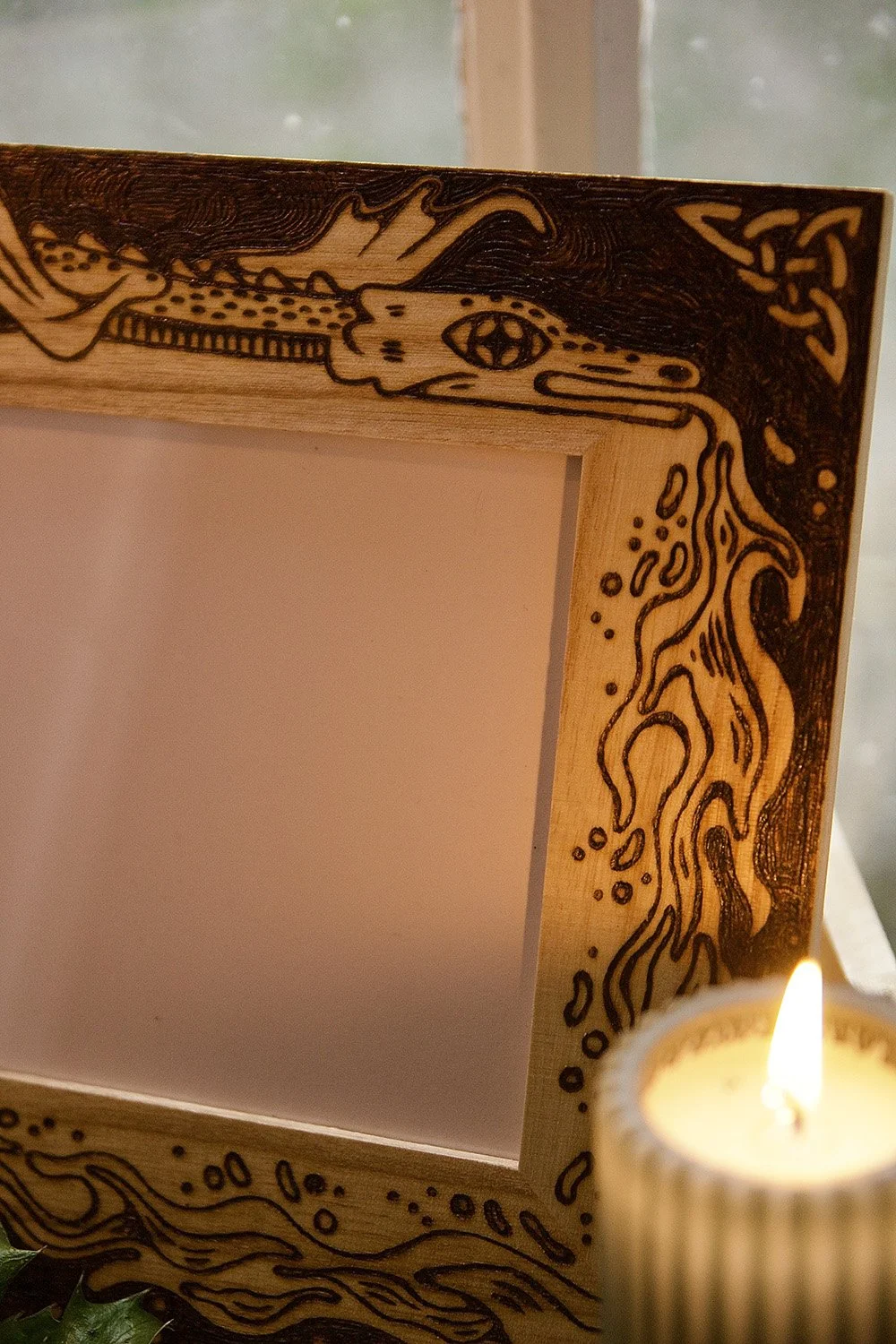 Zoom sur un cadre photo en bois artisanal avec un dragon pyrogravé à la main dans un style médiéval et fantastique.