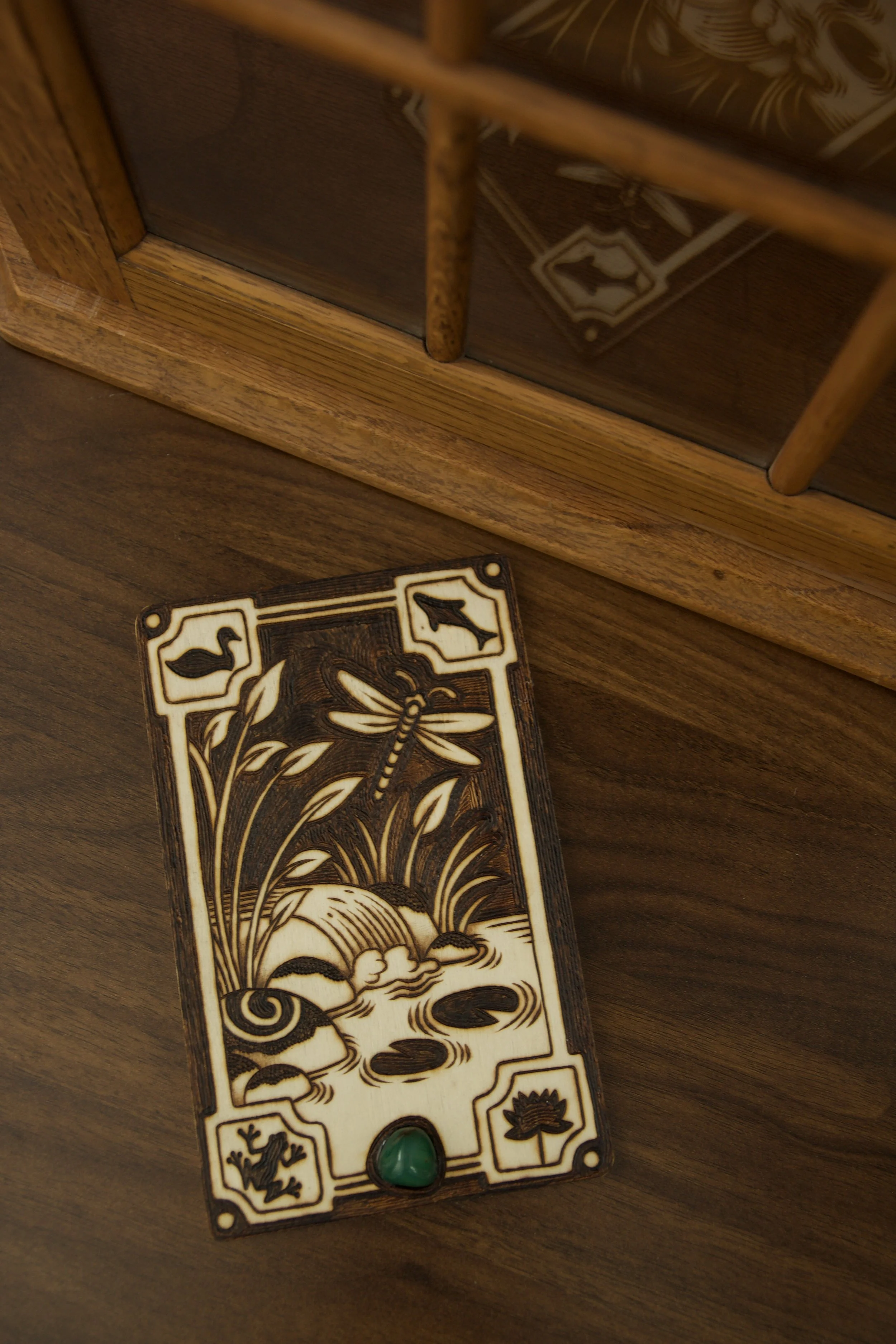 Petite plaque en bois gravée à la main représentant des rivières et la nature sauvage, posée à côté d'une pierre d'aventurine verte naturelle.