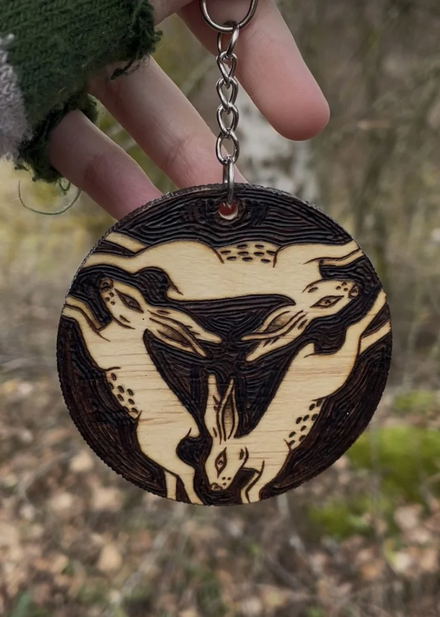 Amulette en bois ronde pyrogravée à la main représentant le symbole mystique et celtique des trois lapins connectés par les oreilles photographié dans dans une forêt.