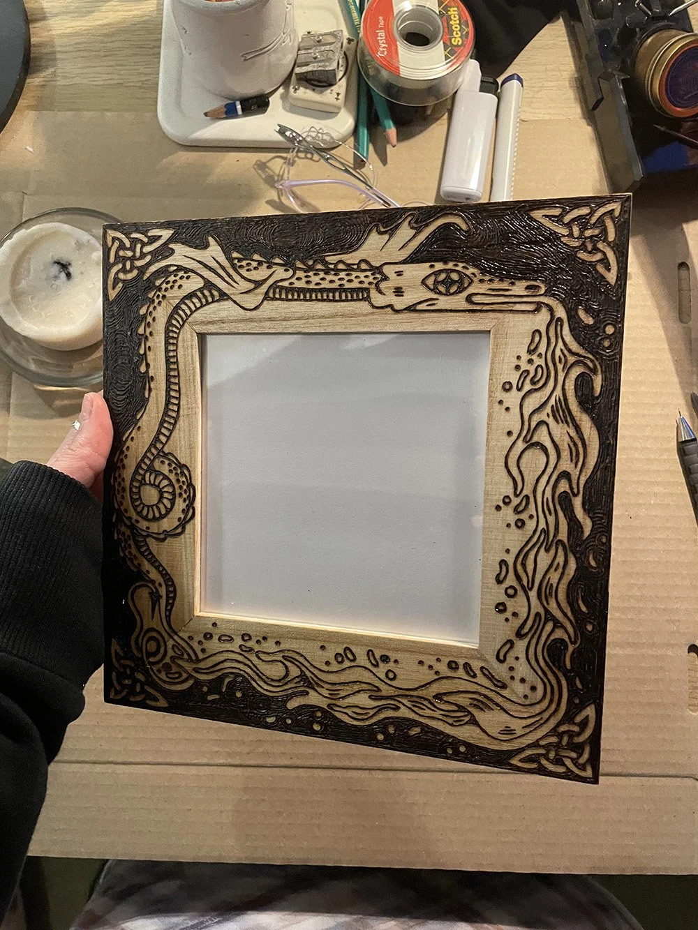 Cadre photo en bois artisanal avec un dragon pyrogravé à la main dans un style médiéval et fantastique dans un atelier d'artiste.