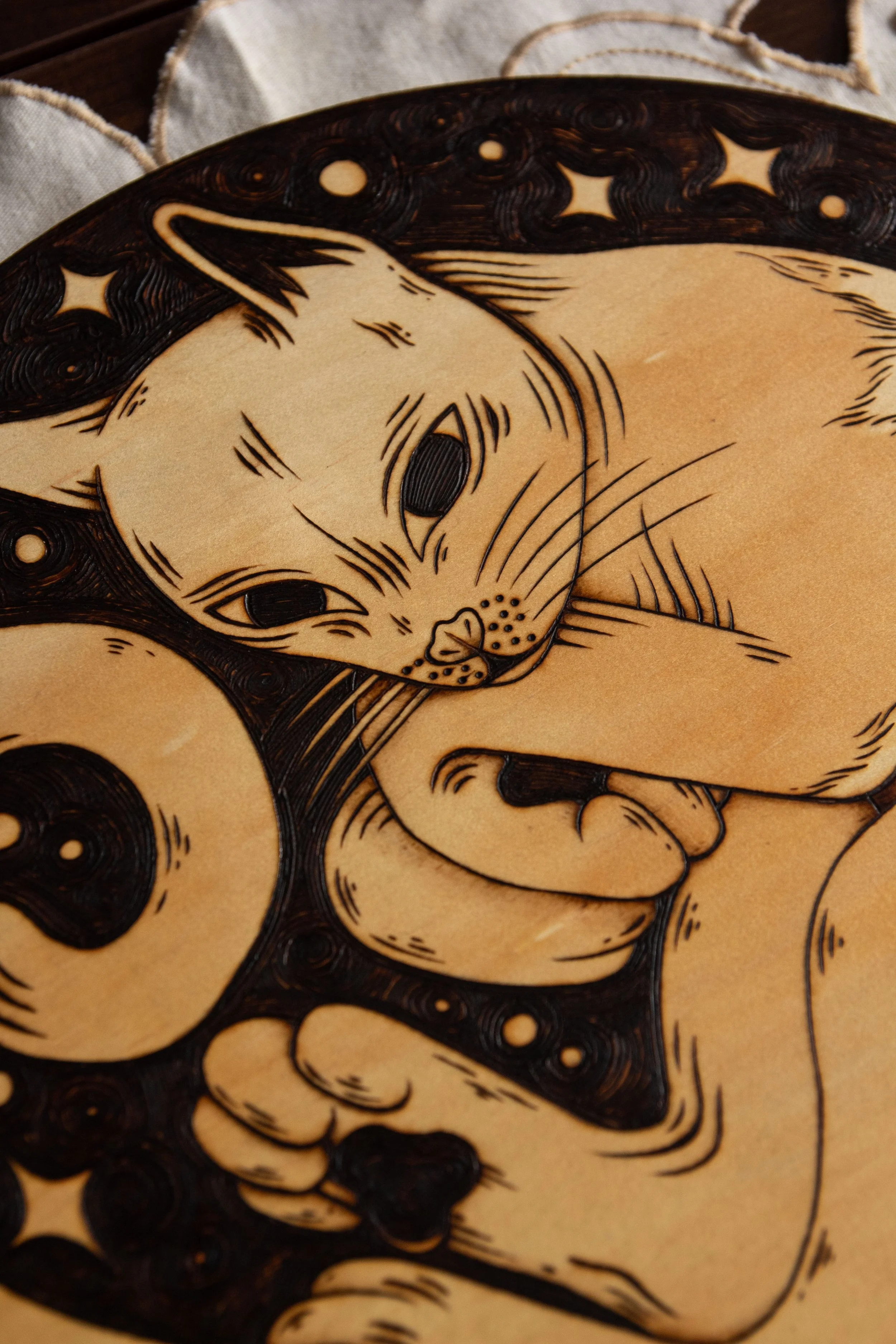 Zoom sur une pyrogravure artisanale sur un disque en bois naturel représentant un chat mystique gravé avec de fins détails de pelage et d'ombrage.