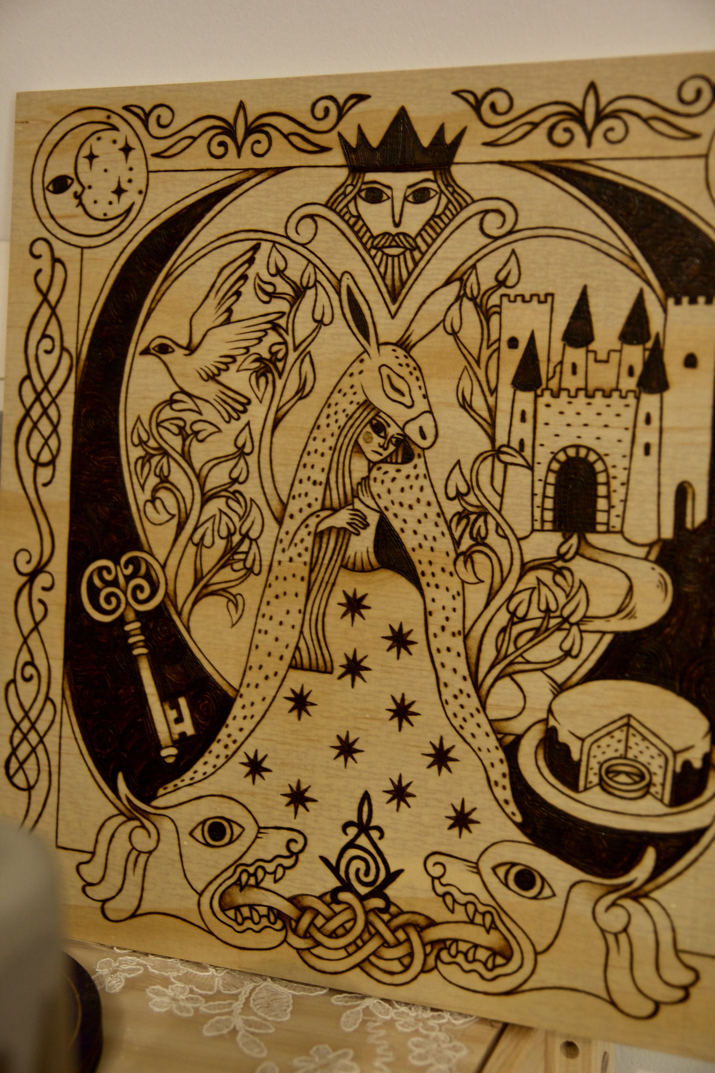 Zoom sur un tableau carré en bois pyrogravé à la main représentant une illustration du conte Peau d’Âne inspirée du style des enluminures médiévales.