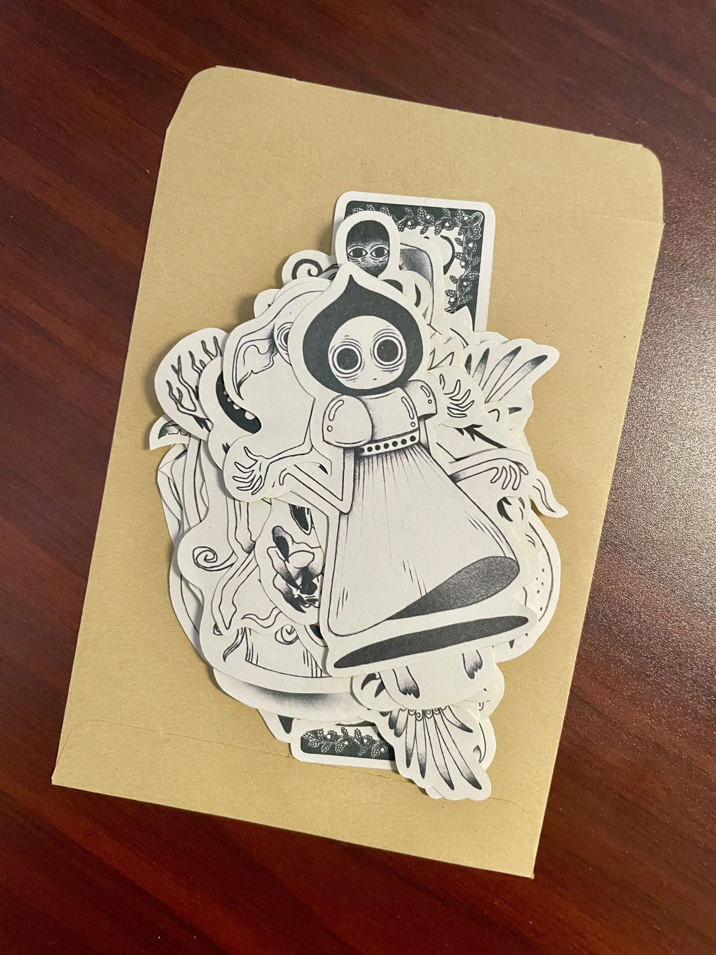 Ensemble de 23 stickers illustrés en noir et blanc de style croquis vintage et mystique, disposés sur un paquet en papier kraft.