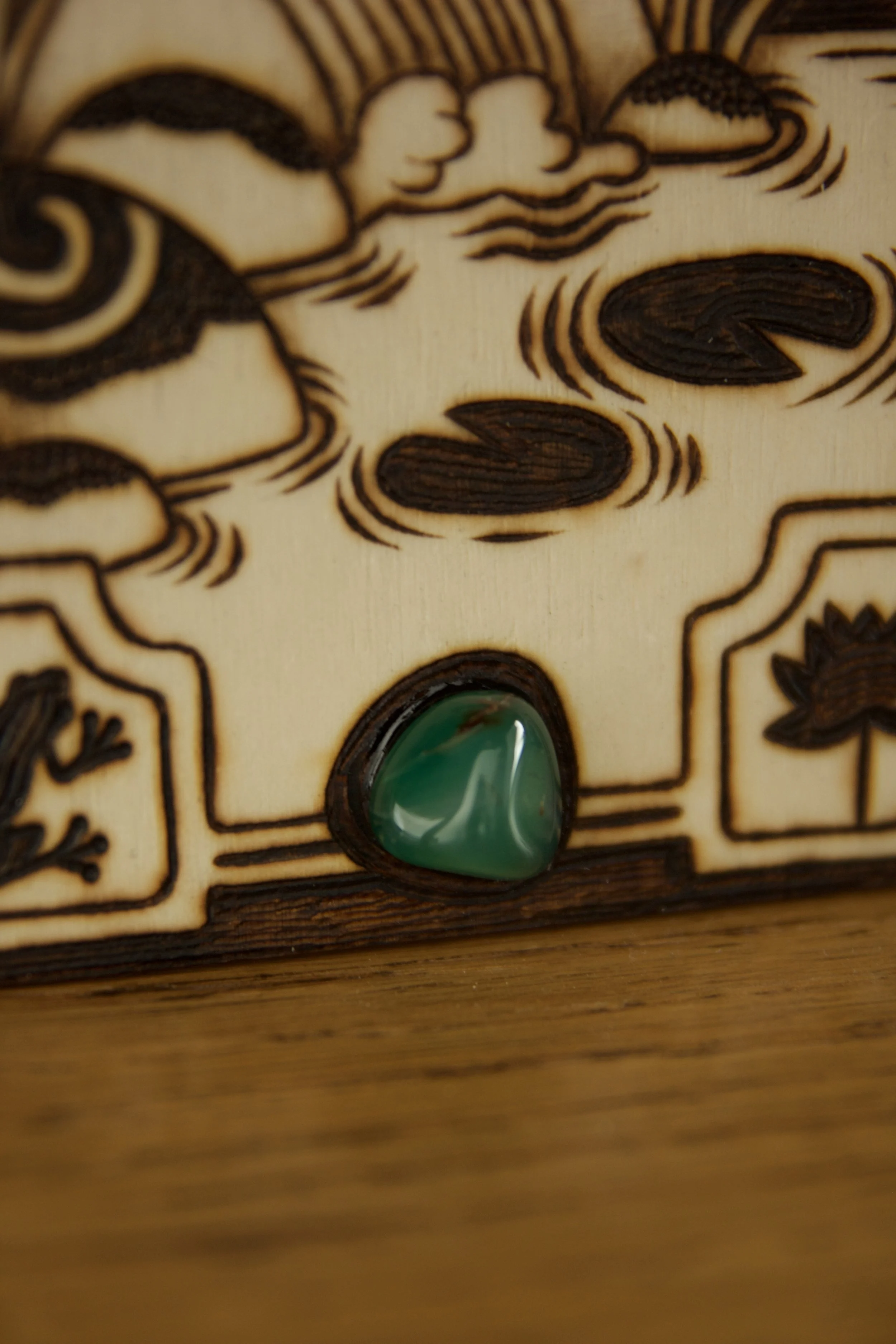 Zoom sur la pierre d'une petite plaque en bois gravée à la main représentant des rivières et la nature sauvage, posée à côté d'une pierre d'aventurine verte naturelle.