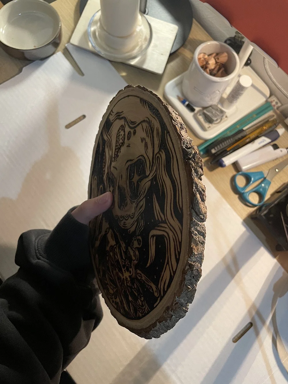 Vue de la tranche d'une pyrogravure artisanale sur bois brut ovale représentant un squelette Memento Mori au style d'un artefact ancien.