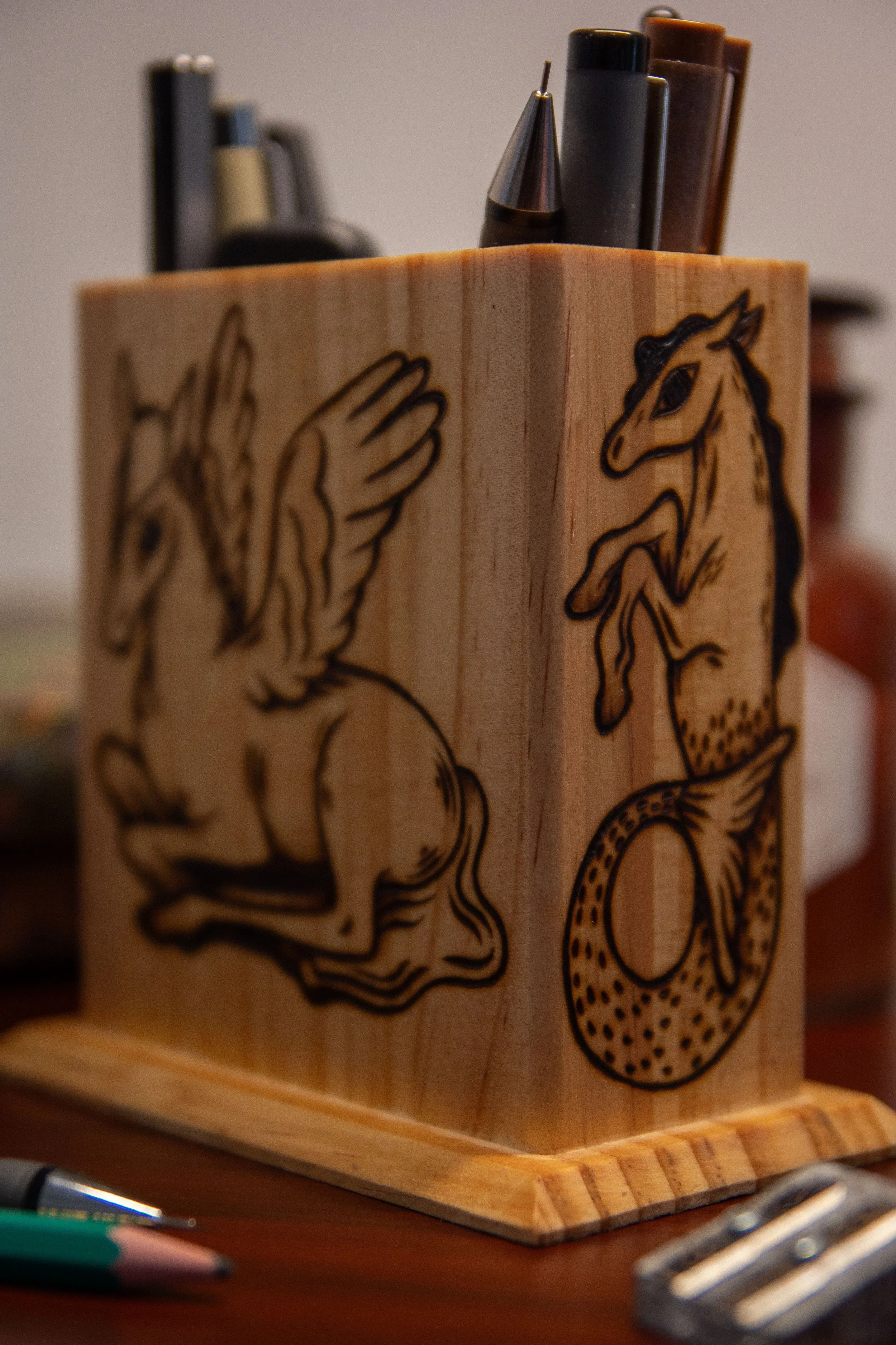 Détail d'un pot à crayons carré en bois artisanal, montrant une face pyrogravée avec soin représentant un cheval magique mystique.
