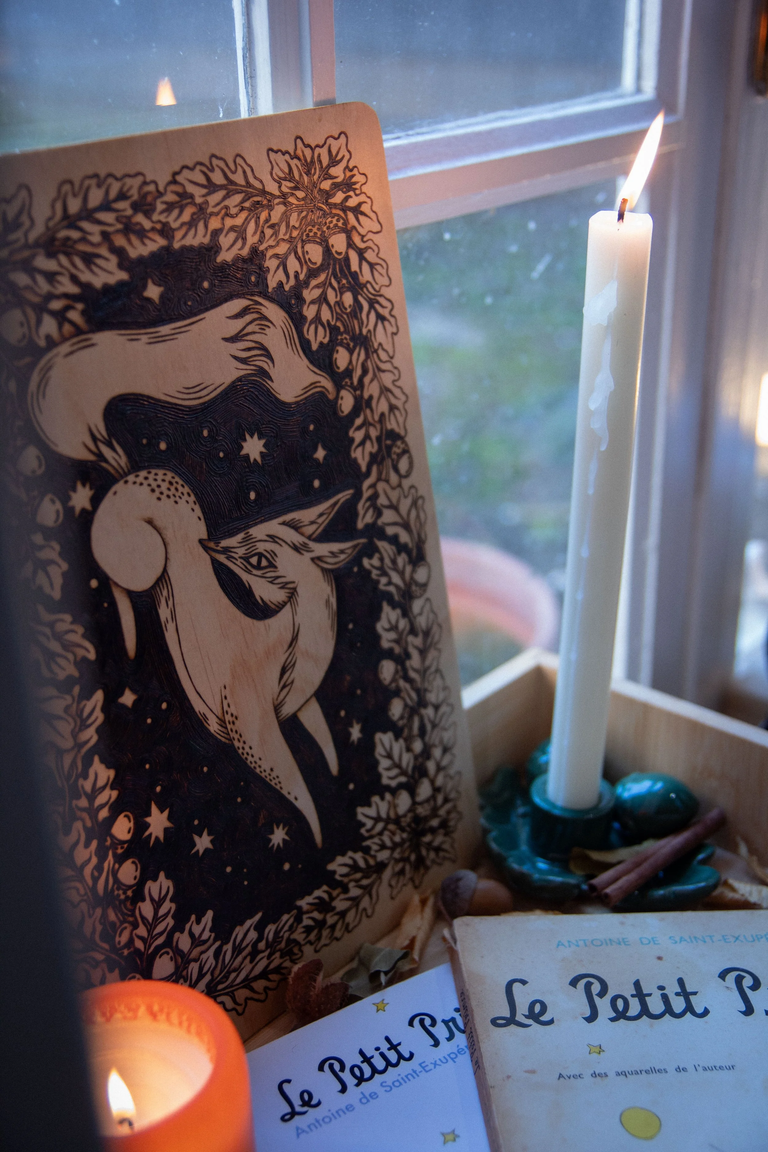 Plaque en bois artisanale finement pyrogravée à la main, représentant un renard mystique aux détails ombrés au cœur de la forêt devant une fenêtre et une bougie.