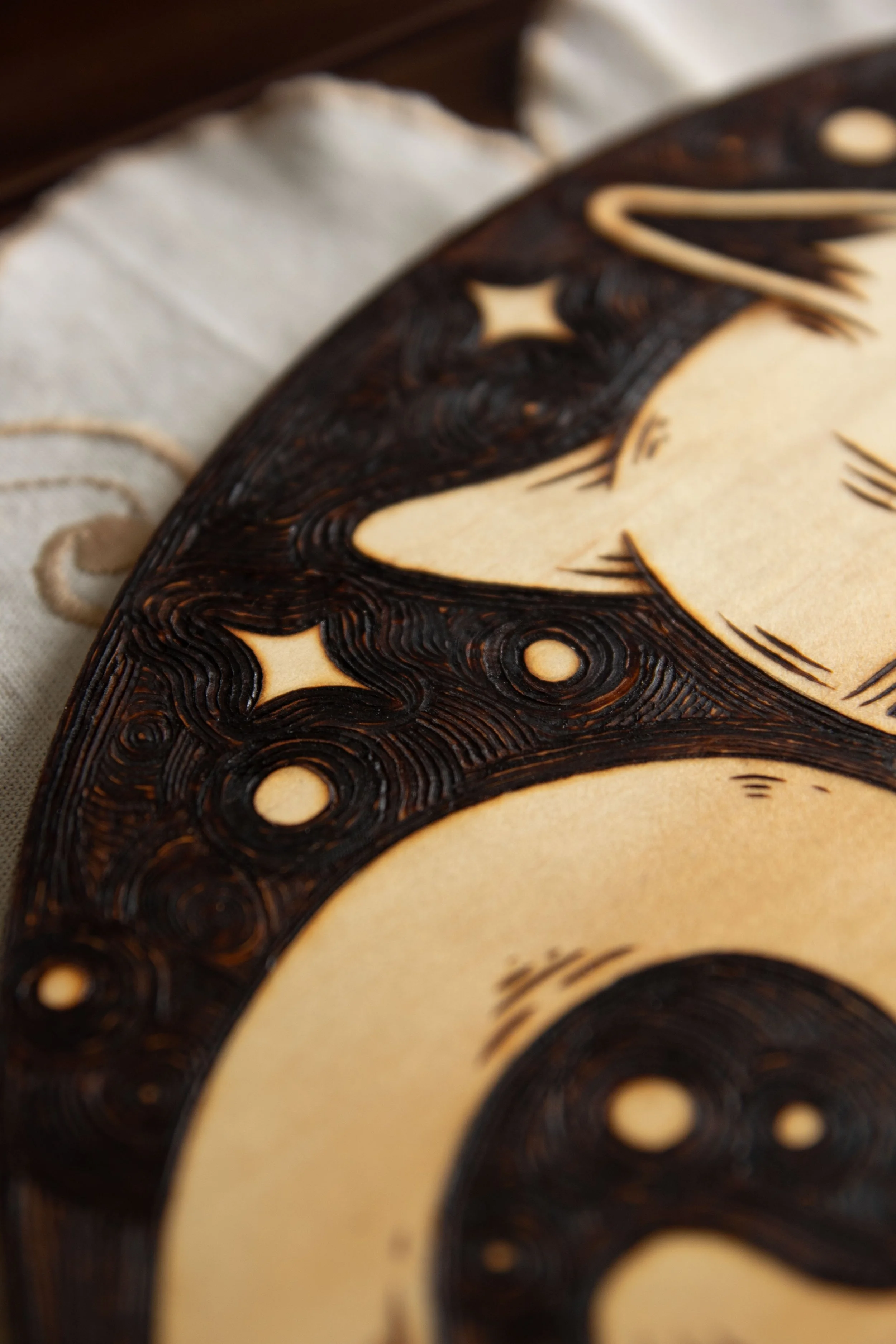 Détail des traits de gravure d'une pyrogravure artisanale sur un disque en bois naturel représentant un chat mystique gravé avec de fins détails de pelage et d'ombrage.