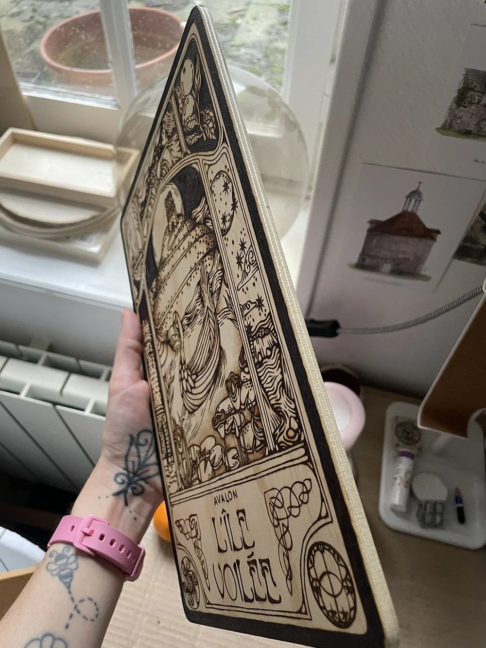 Vue de la tranche d'une pyrogravure artisanale sur planche de bois évoquant une illustration ancienne de l'île mythique d'Avalon dans la brume.